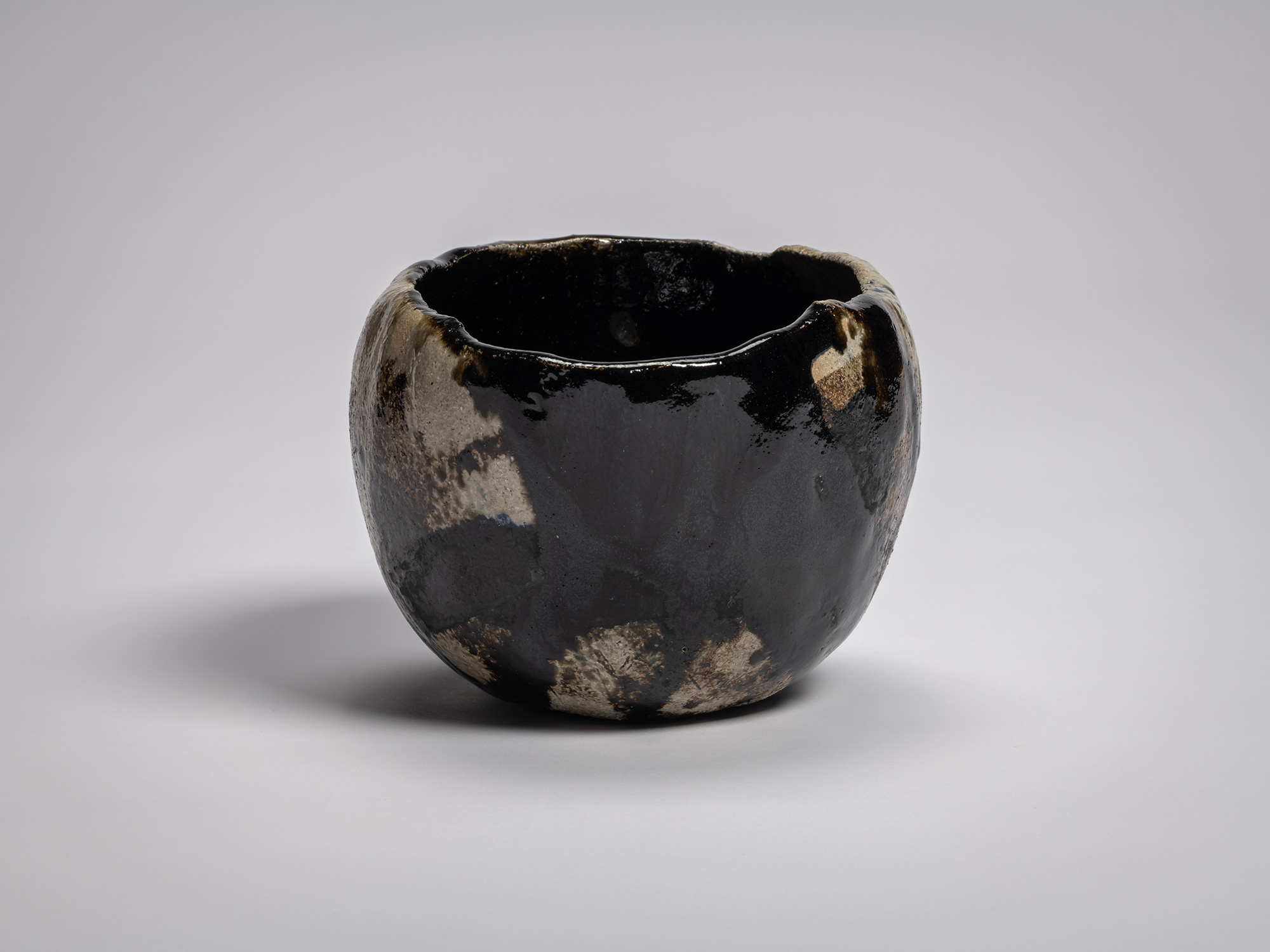 Side profile of black raku tea bowl by Raku XV titled Hatō (Great Wave in Ocean), featuring an...