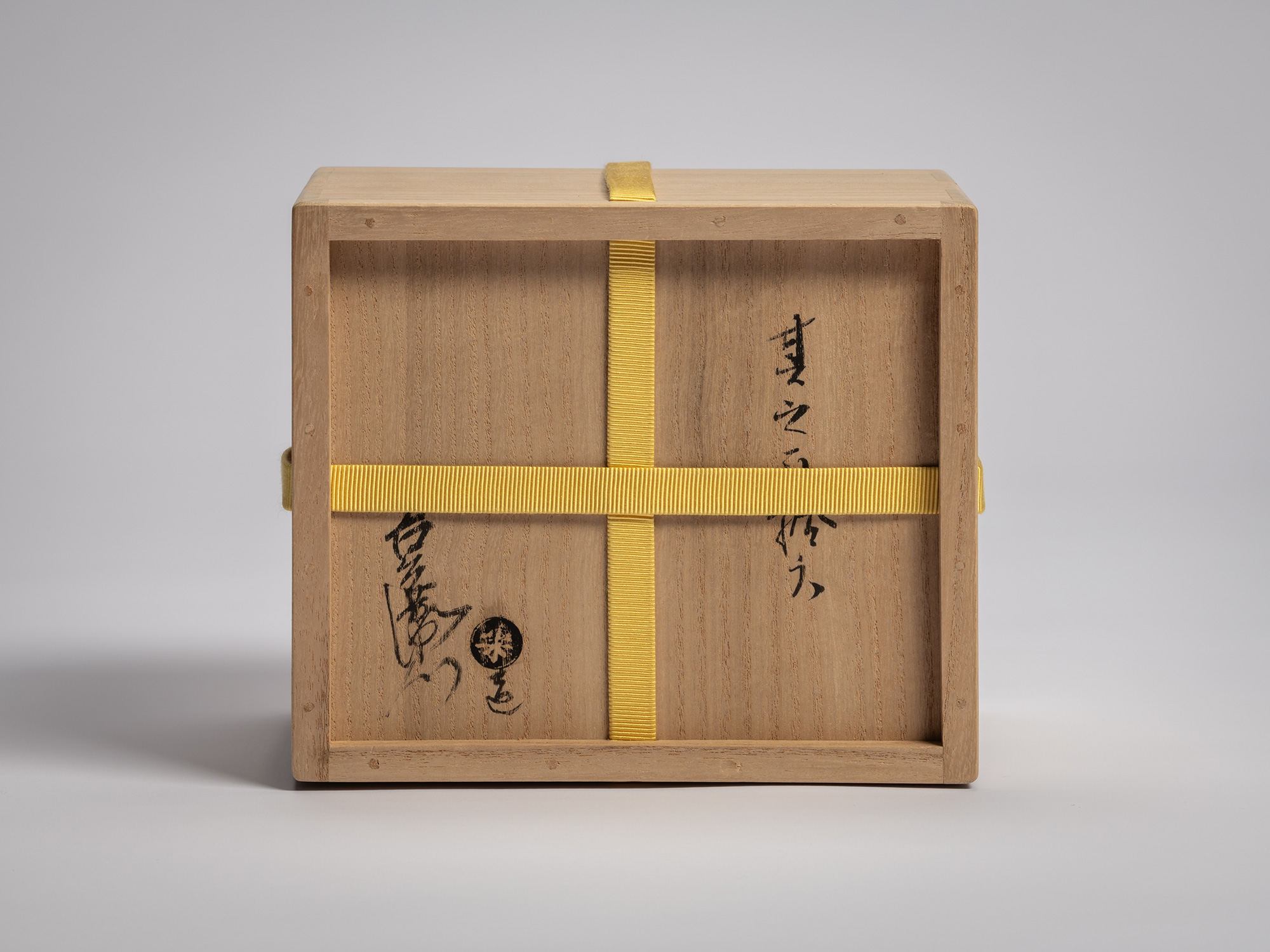 Underside of the paulownia wood tomobako secured with a yellow cord, bearing handwritten ink inscription...
