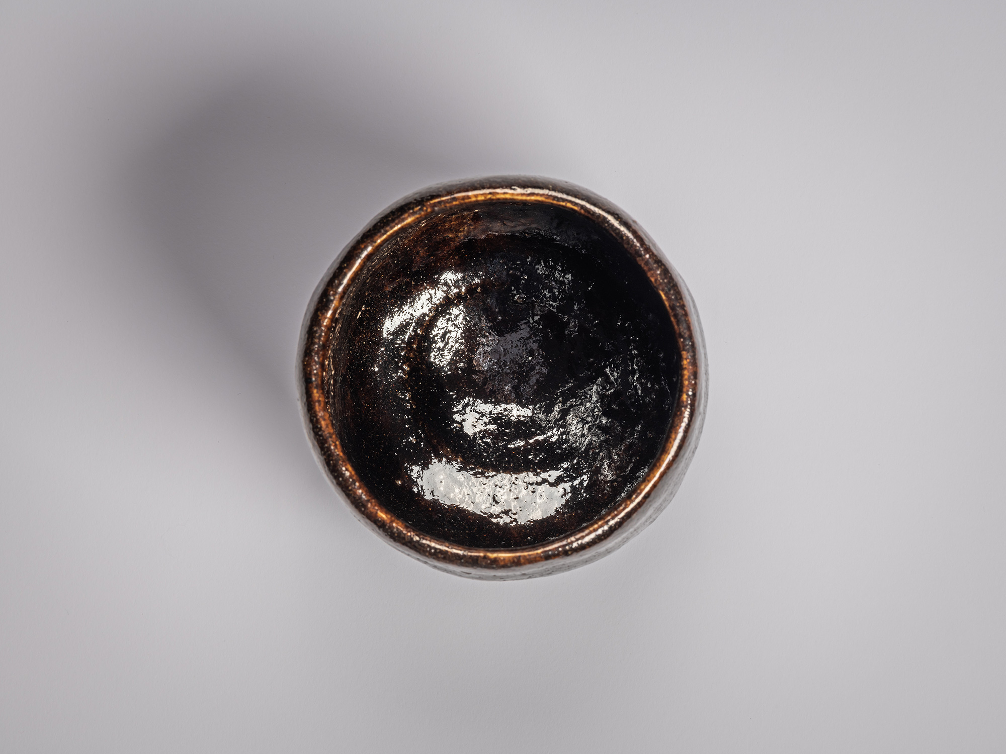 Overhead view of the cup’s interior showing a glossy, dark brown to black glaze pooling toward...