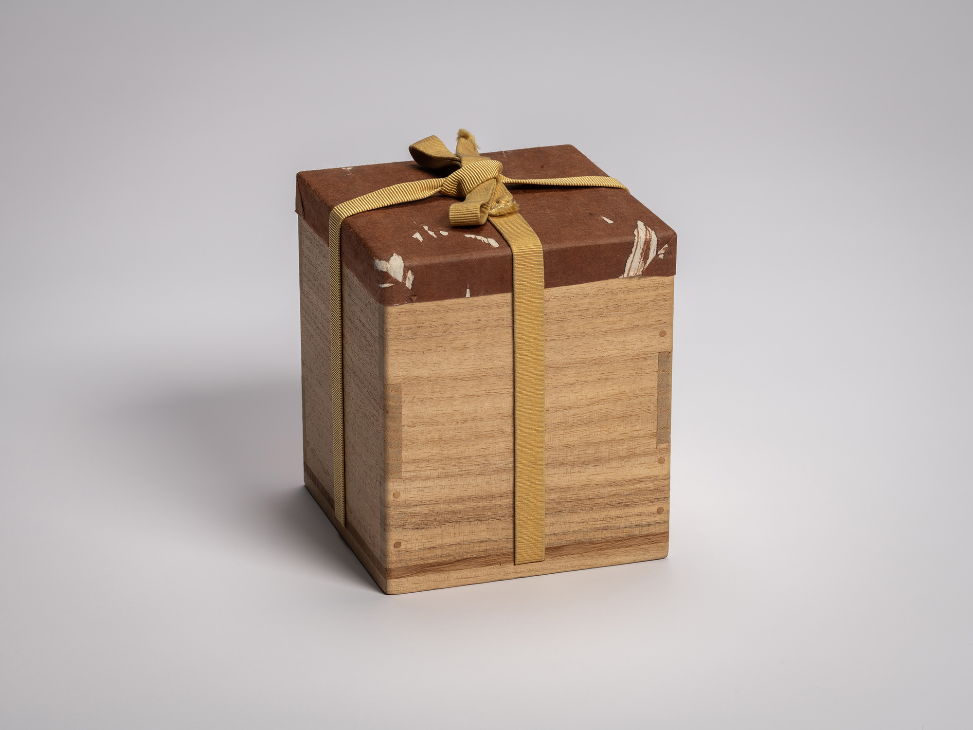 Kiri wood storage box wrapped in brown protective paper and tied with yellow silk ribbon; lid and...