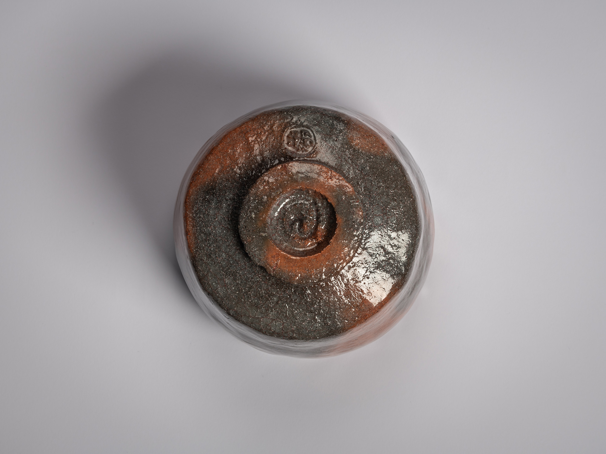 Foot of a Red Raku tea bowl by Raku XVI, showing a circular trimmed foot ring with pooled red and...