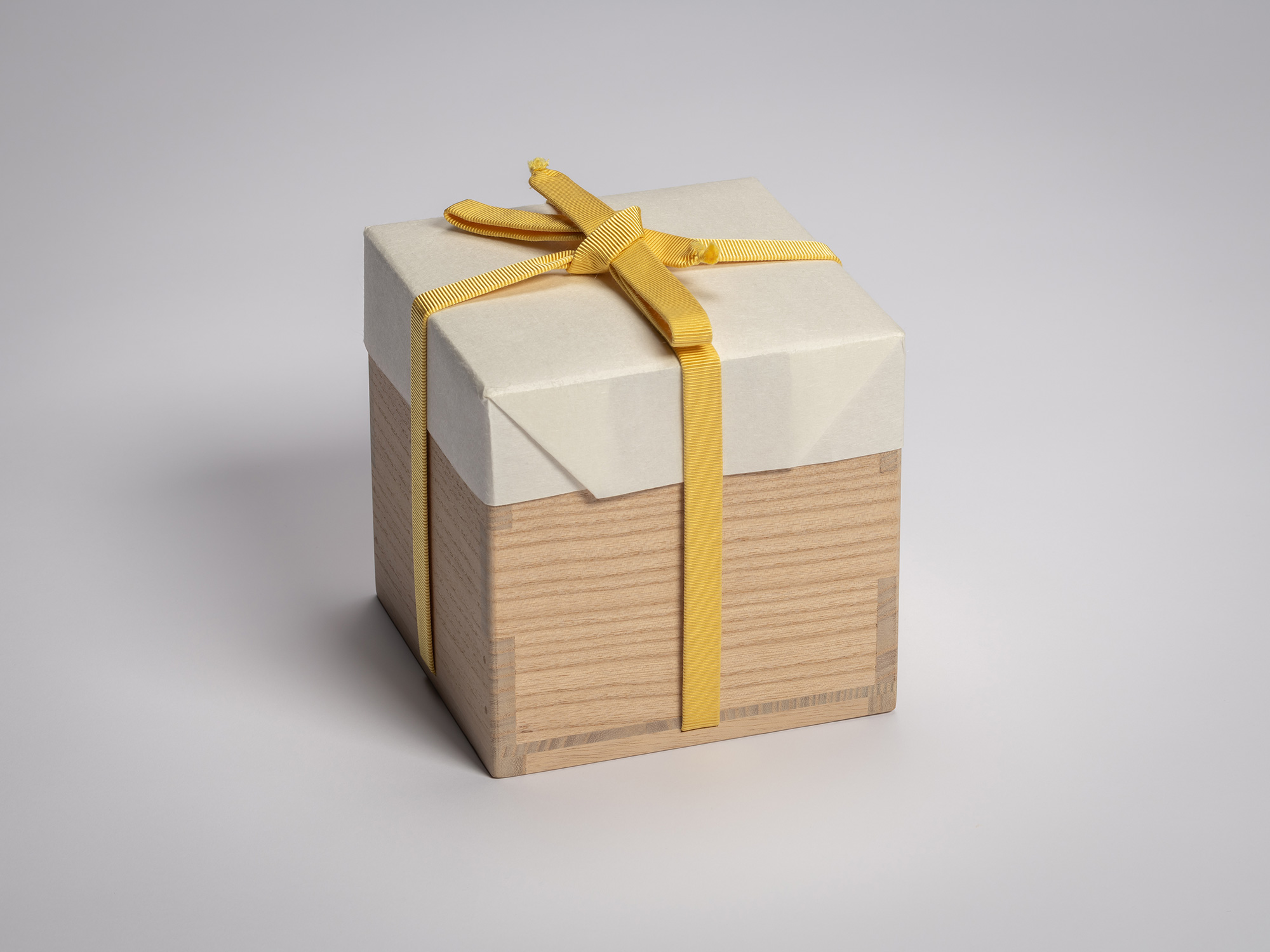 Wooden artist box containing a red tea bowl by Raku XVI, tied with a yellow cord and topped with...