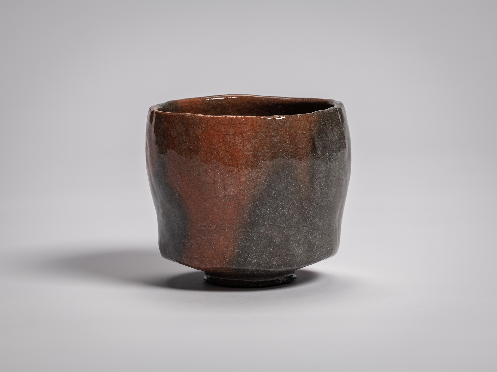 Red Raku tea bowl by Raku XVI, featuring a softly faceted cylindrical form with a gently uneven...