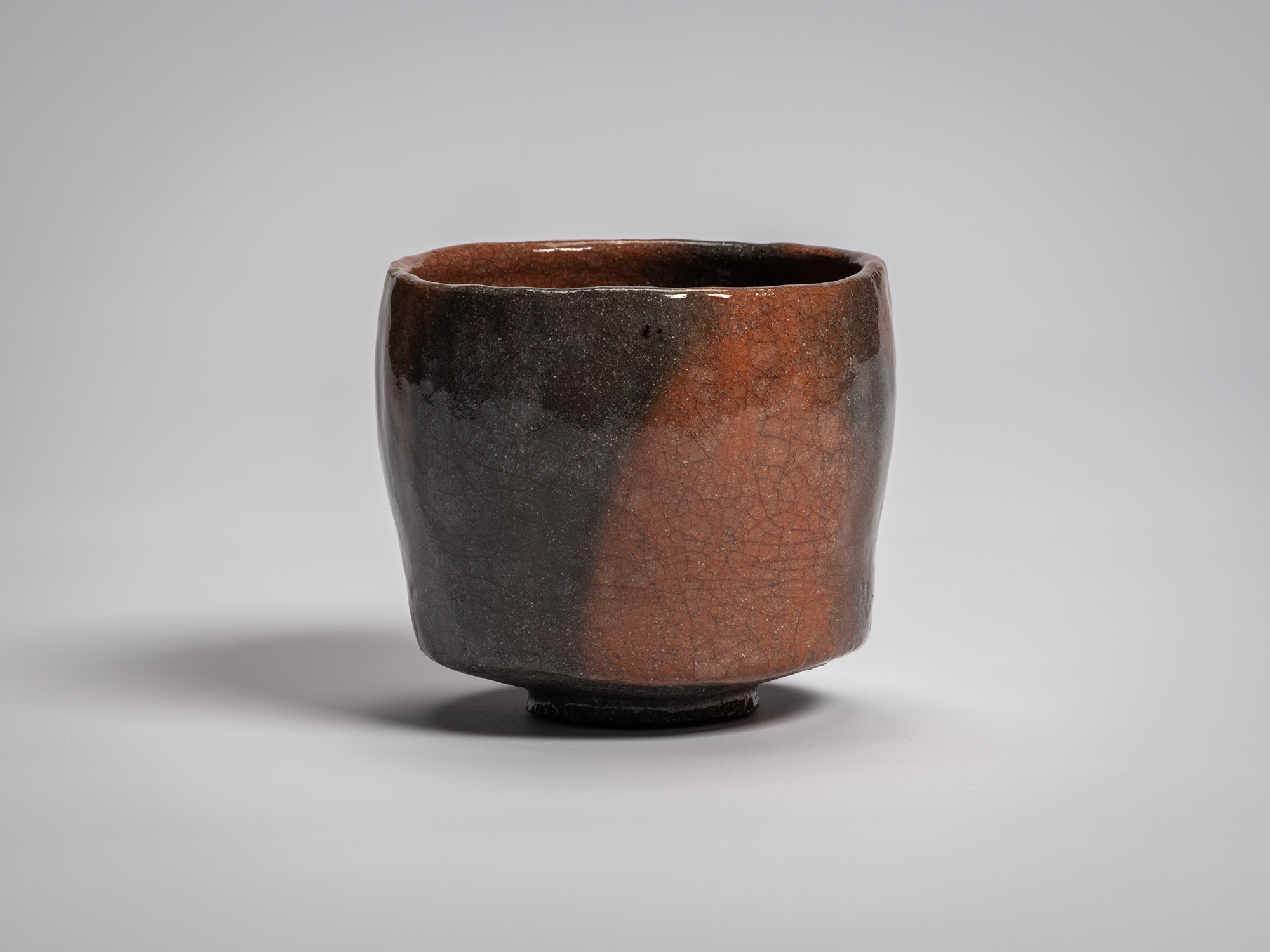 Red Raku tea bowl by Raku XVI, featuring a softly faceted cylindrical form with a gently uneven...