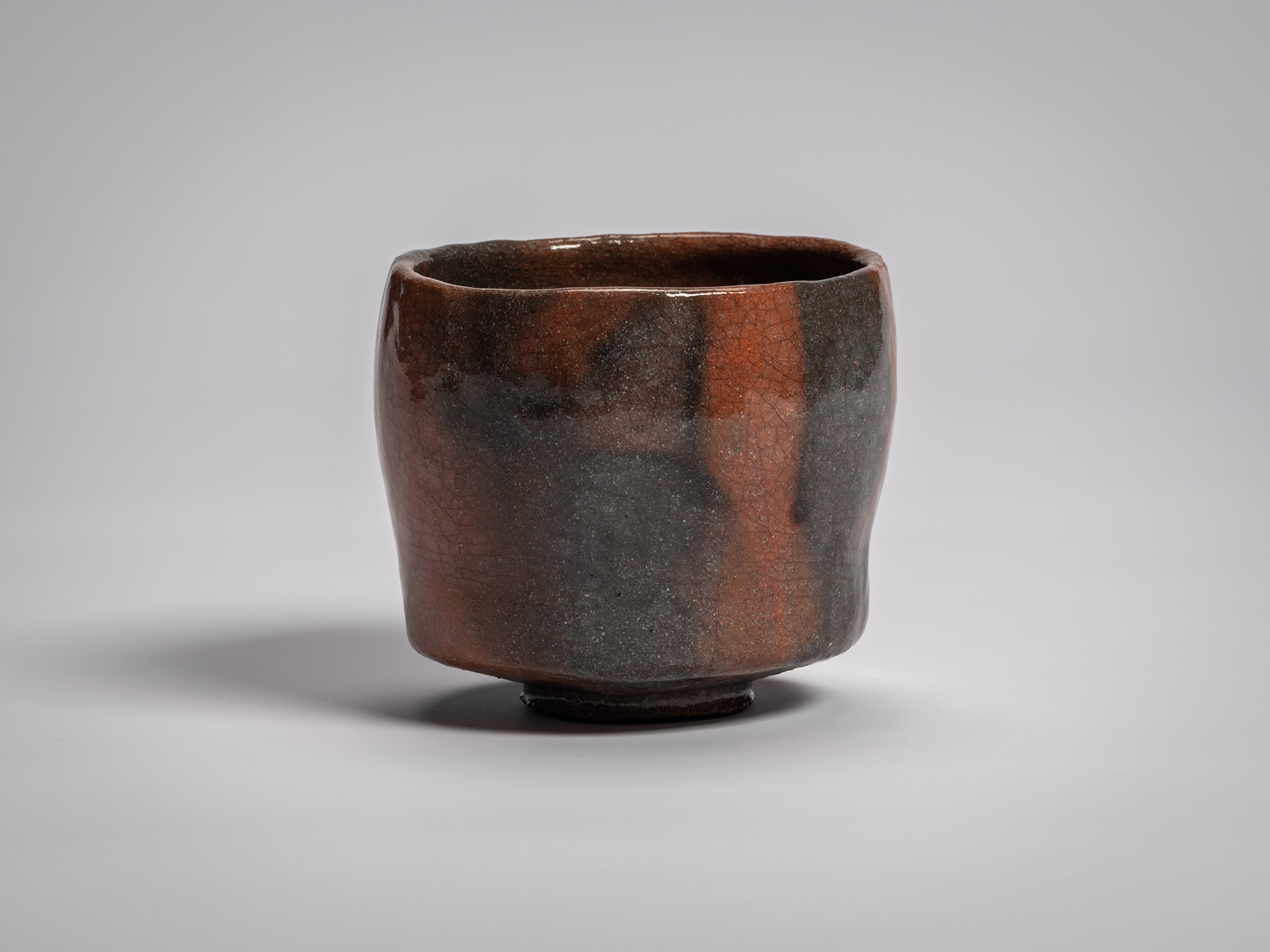 Red Raku tea bowl by Raku XVI, featuring a softly faceted cylindrical form with a gently uneven...