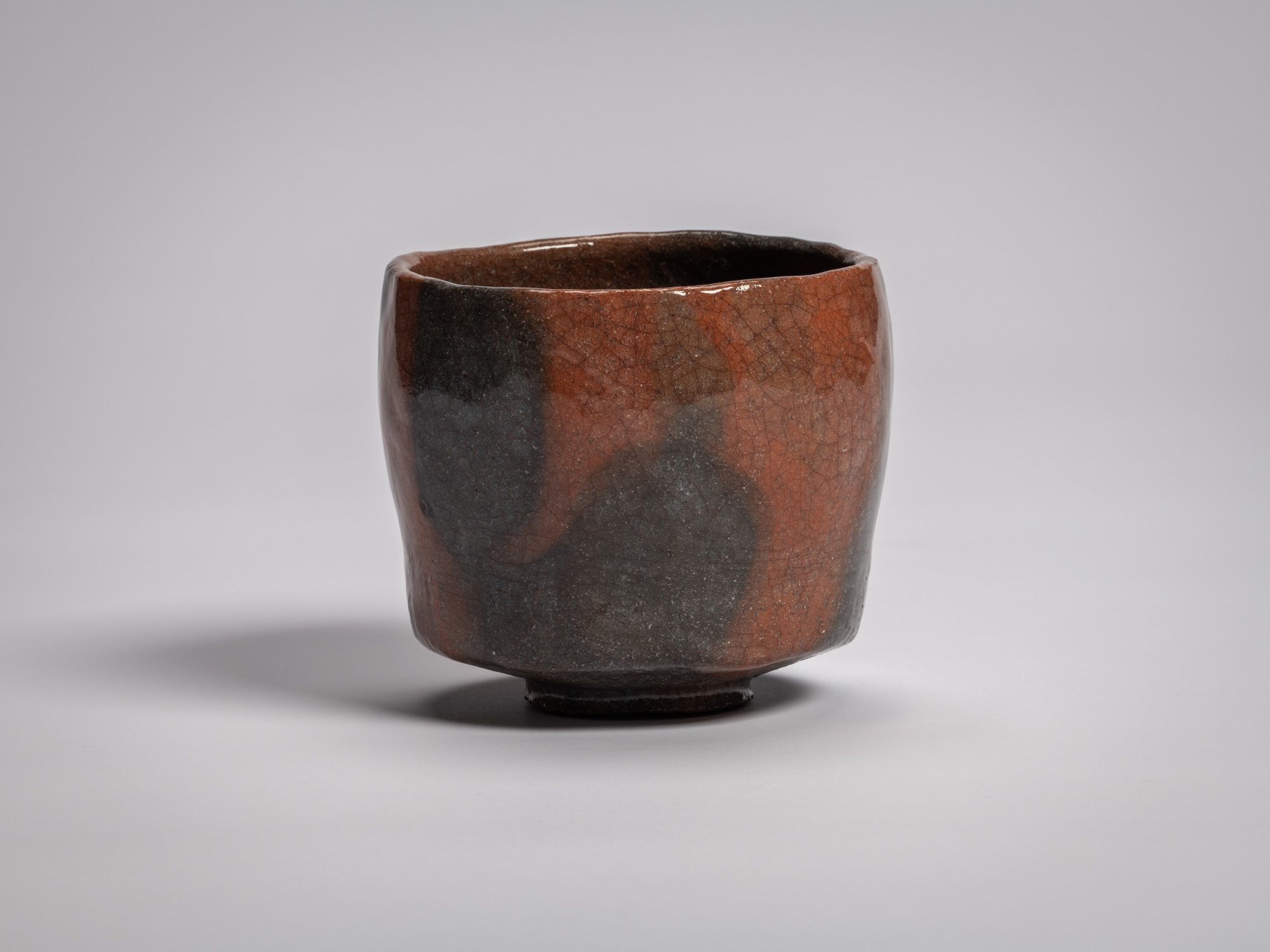 Red Raku tea bowl by Raku XVI, featuring a softly faceted cylindrical form with a gently uneven...