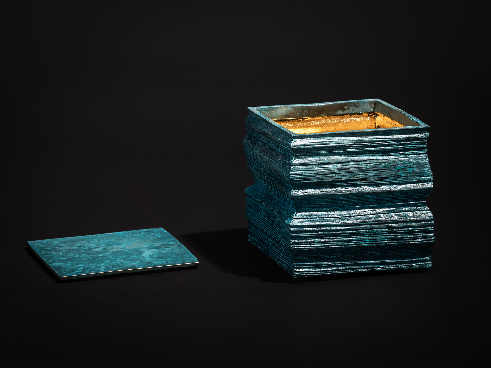 Square Strips bronze box shown open, with the square lid placed to the side. The exterior is built...