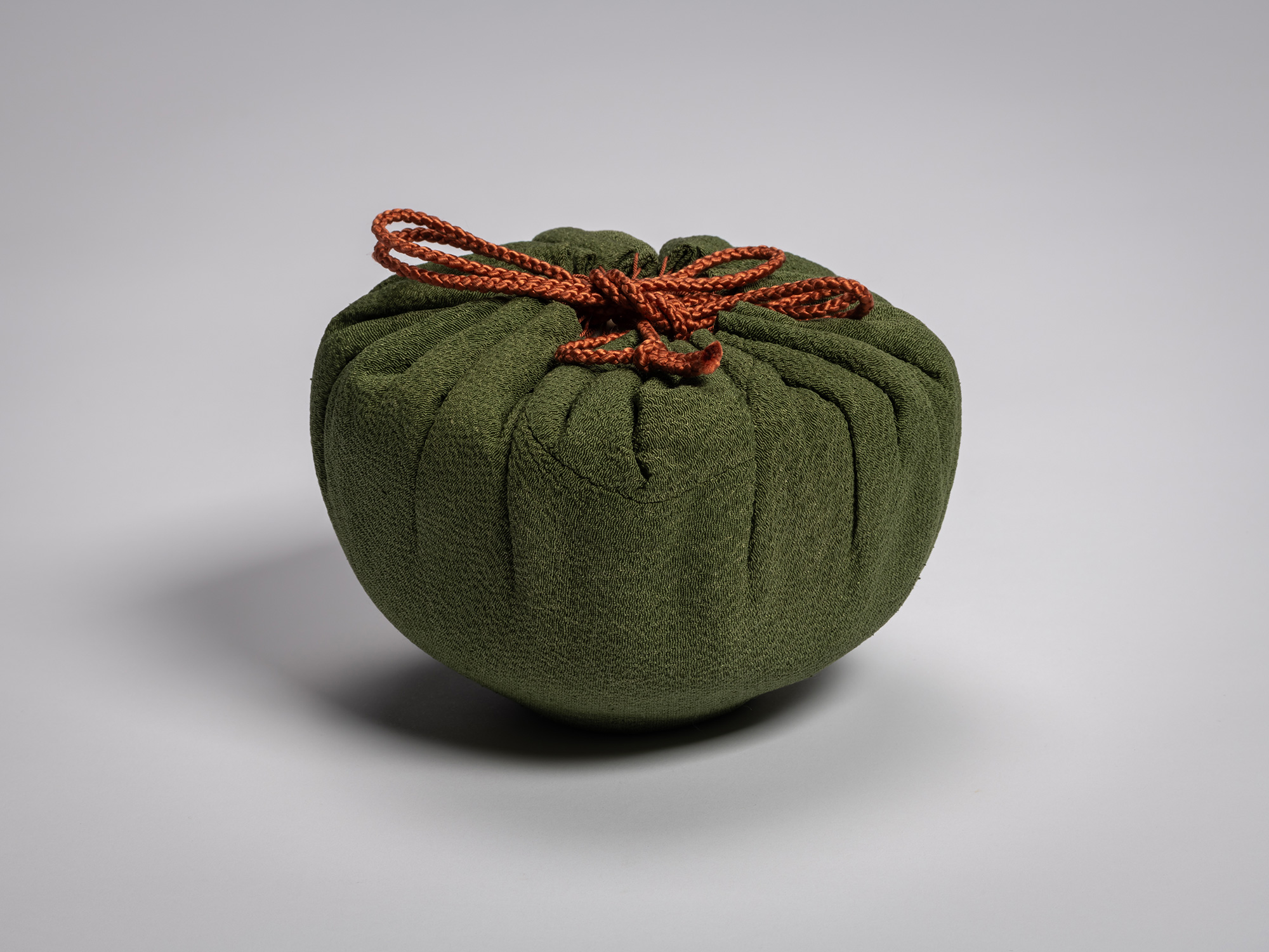 The tea bowl Yōbō Shungen by Raku IX wrapped in a deep green silk cloth, gathered into soft folds...