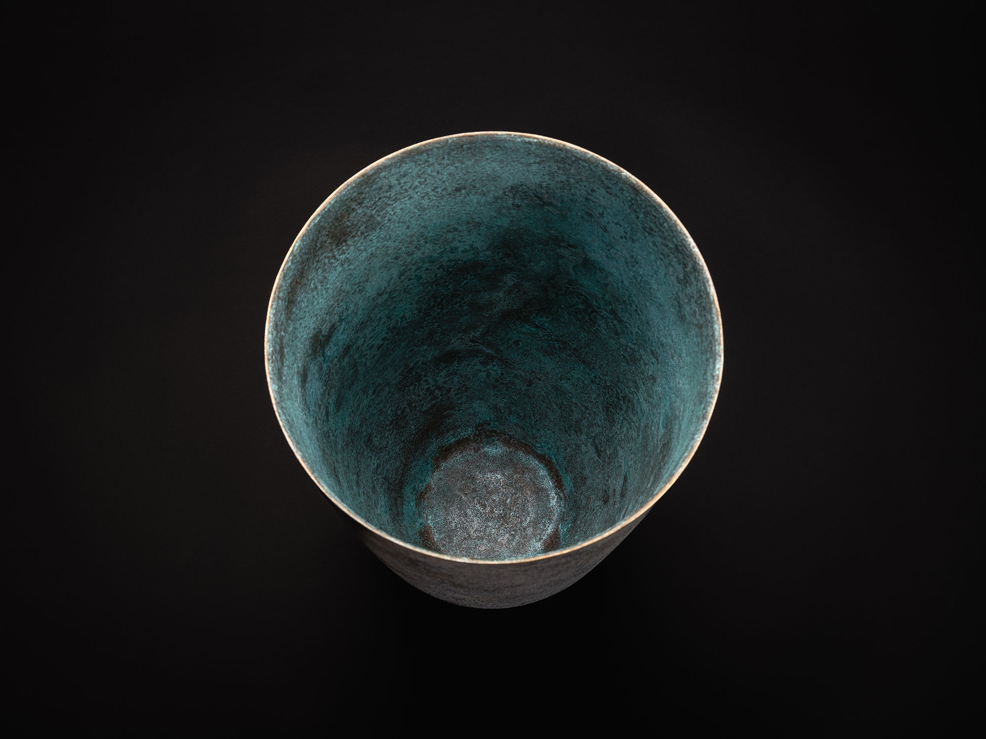 Top view looking into a tall bronze vase by Koji Hatakeyama. The vessel has a wide circular opening...