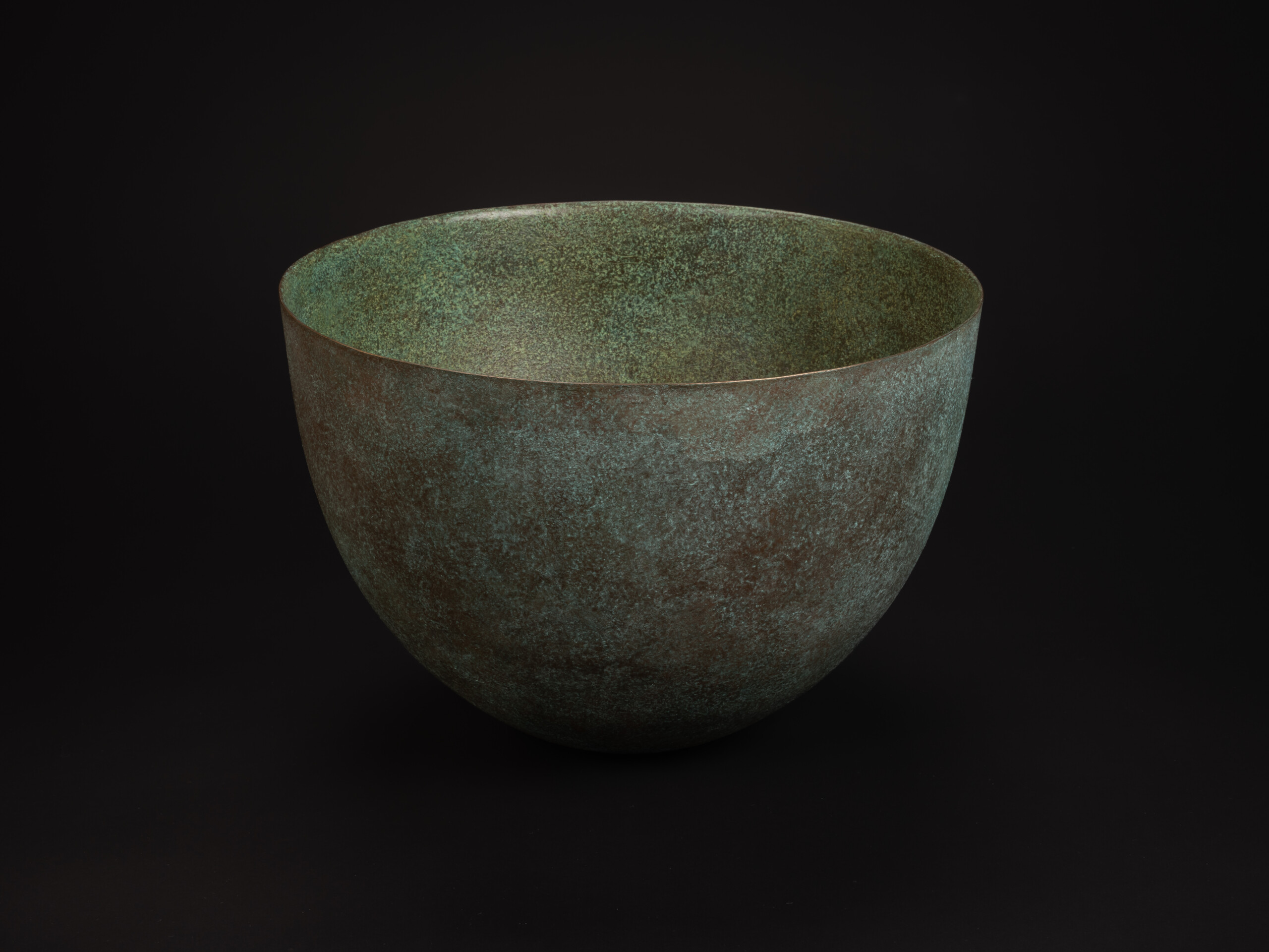 Rounded bronze vessel titled Bronze No. 17 by Hatakeyama set against a dark background, with a...