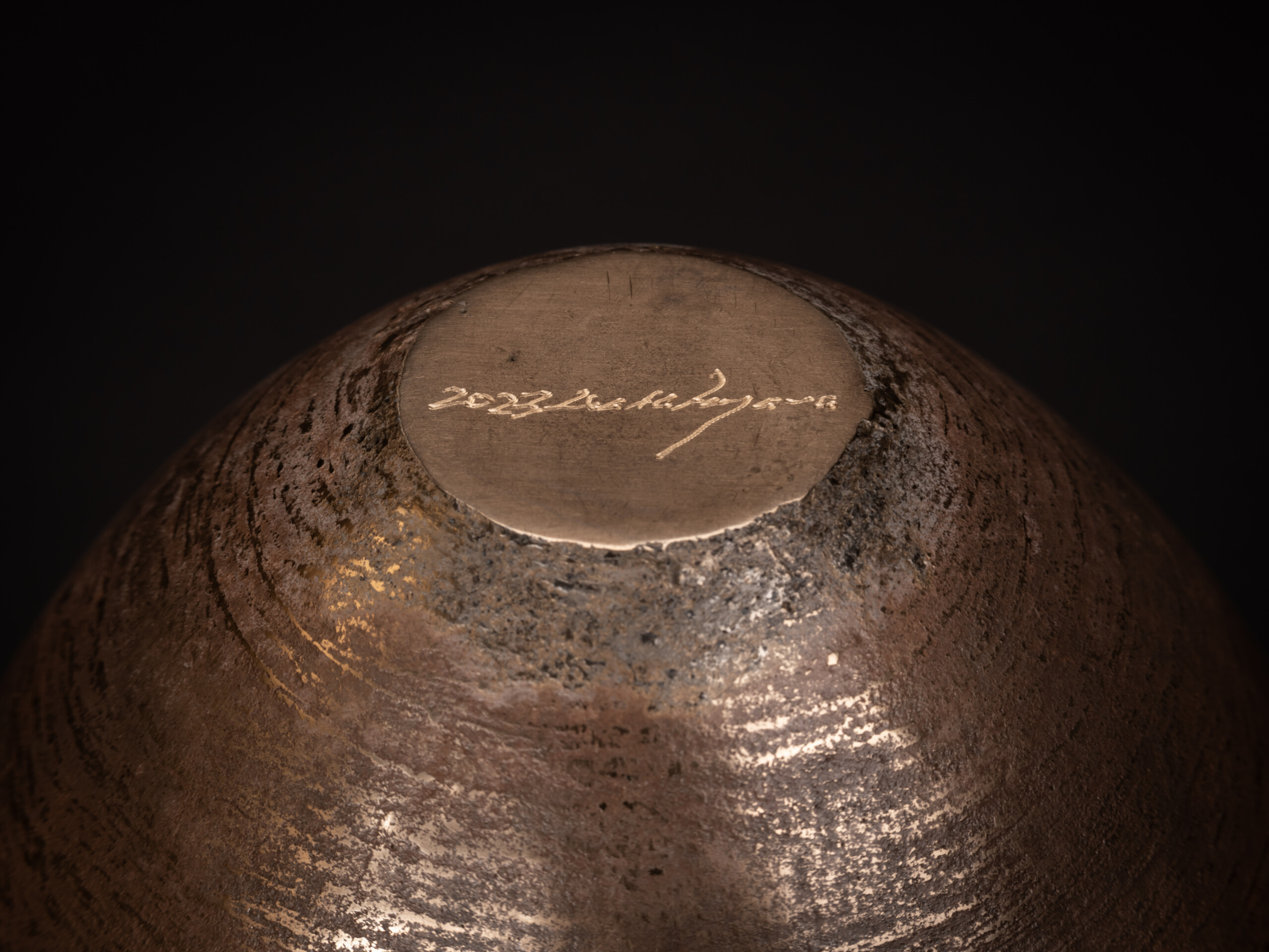 Underside view of a bronze bowl by Koji Hatakeyama showing a circular base with a smooth, slightly...