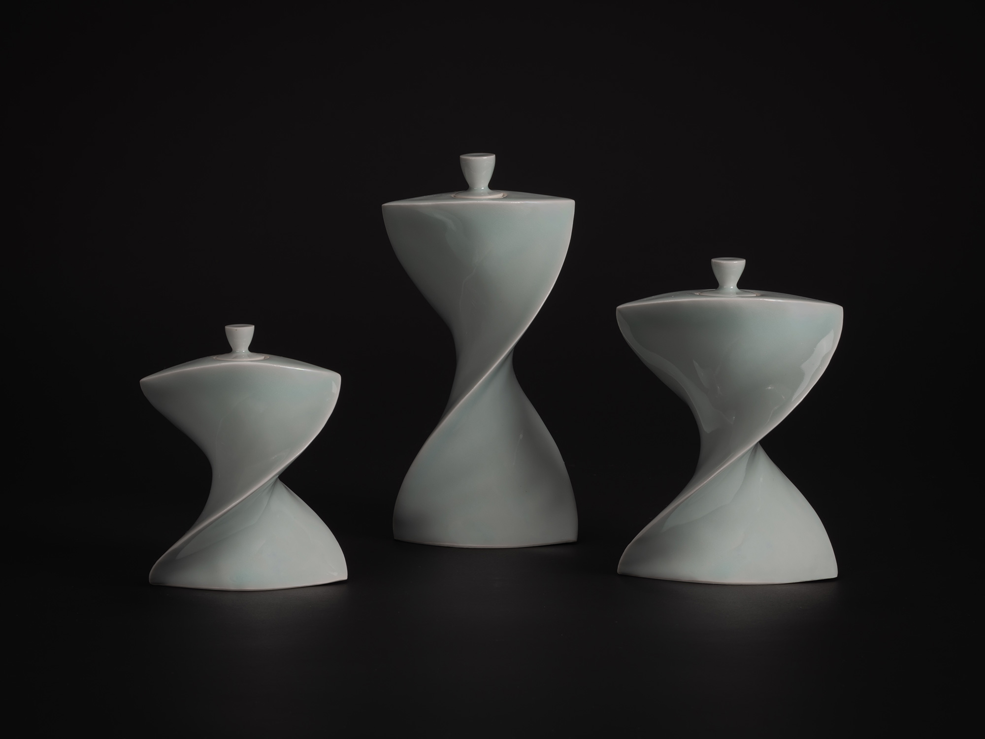 Three white porcelain Faceted Covered Vessels by Akira Yagi, each with a twisting hourglass form...