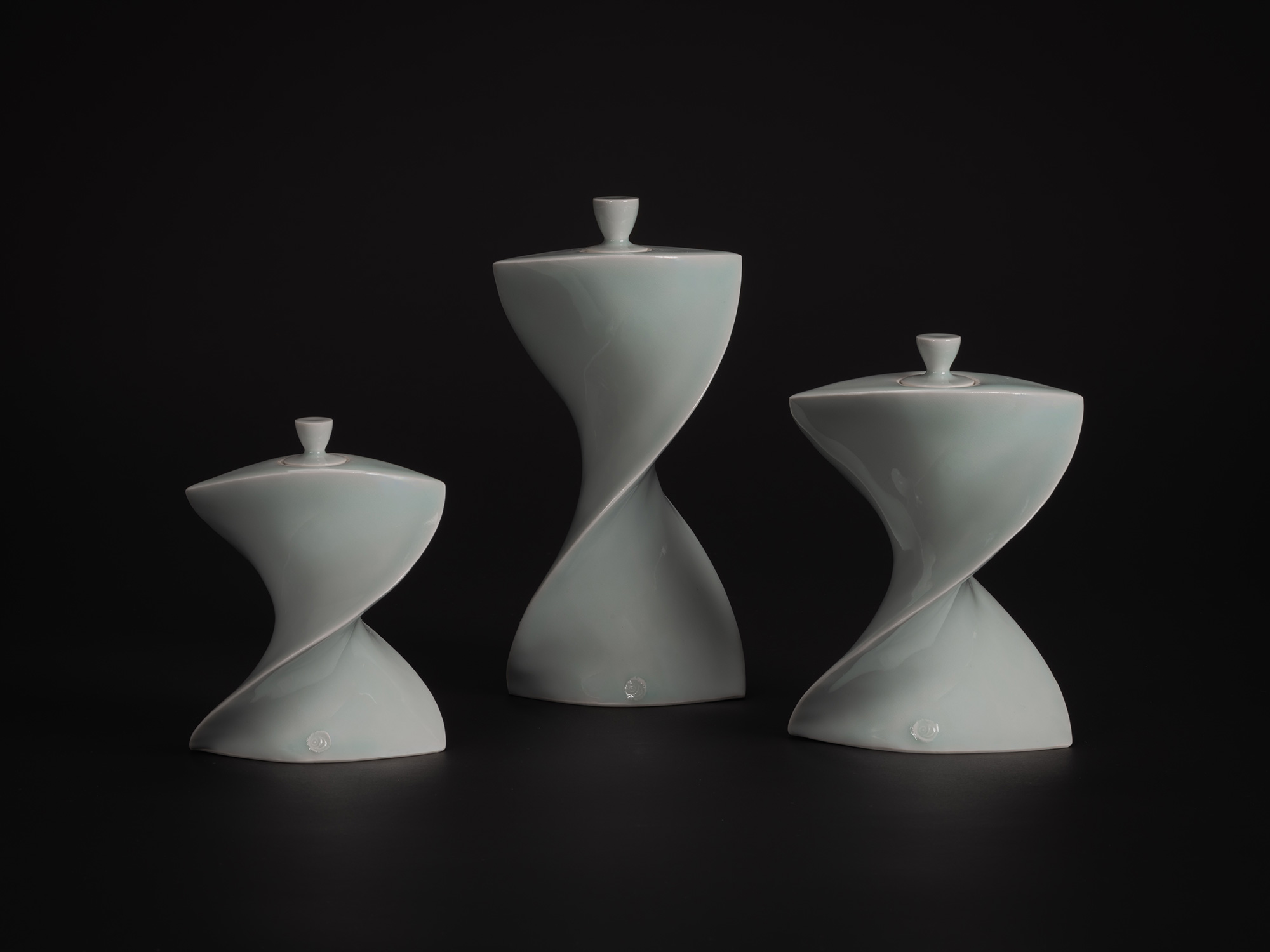 Three white porcelain Faceted Covered Vessels by Akira Yagi, each with a twisting hourglass form...