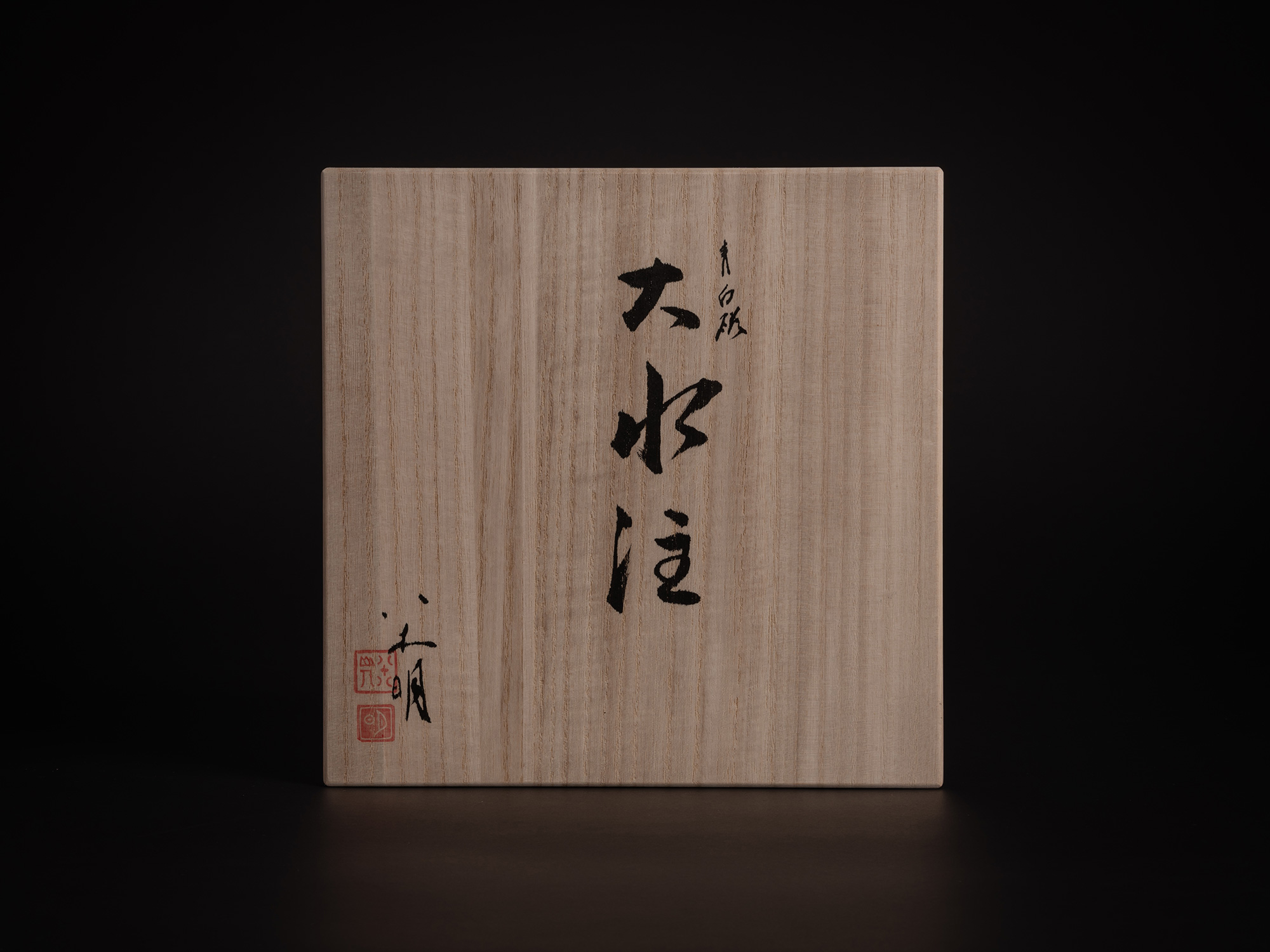 A top-down, centered photograph of the tomobako (traditional Japanese wooden storage box) lid for...