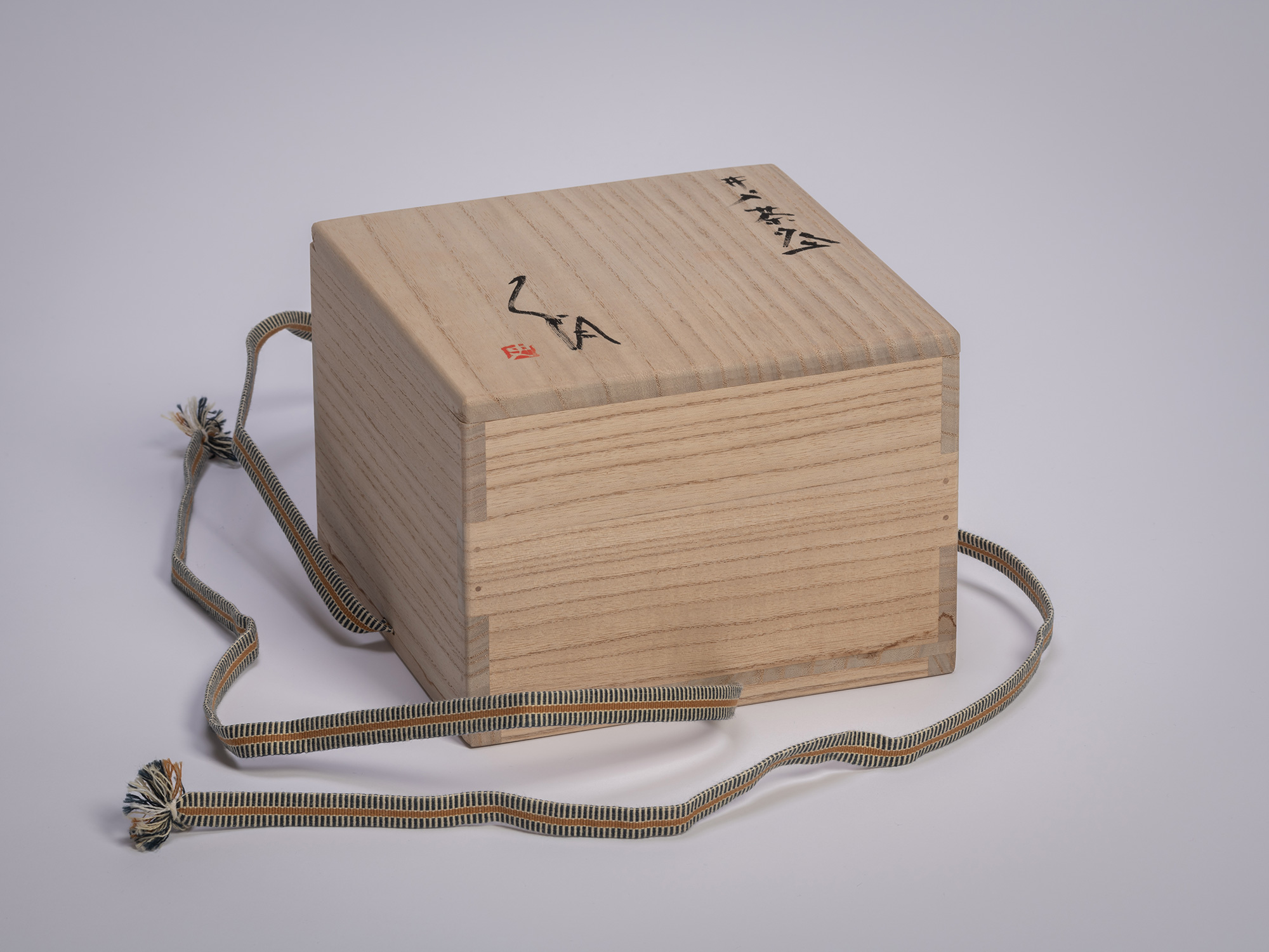 Wooden tomobako storage box for an Ido chawan by Tsujimura, showing a light wood grain surface...