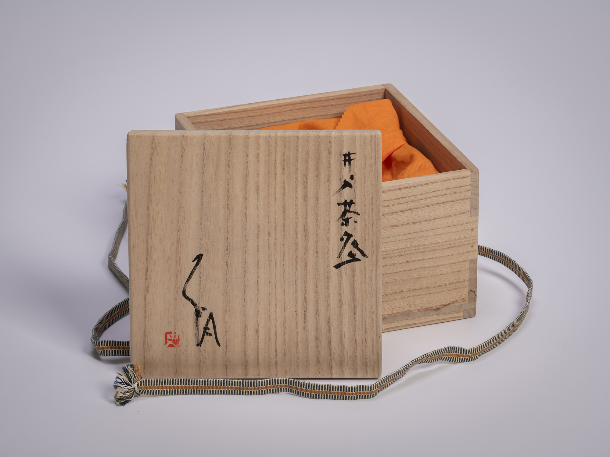 Wooden tomobako storage box for an Ido chawan by Tsujimura, shown open to reveal an orange cloth...