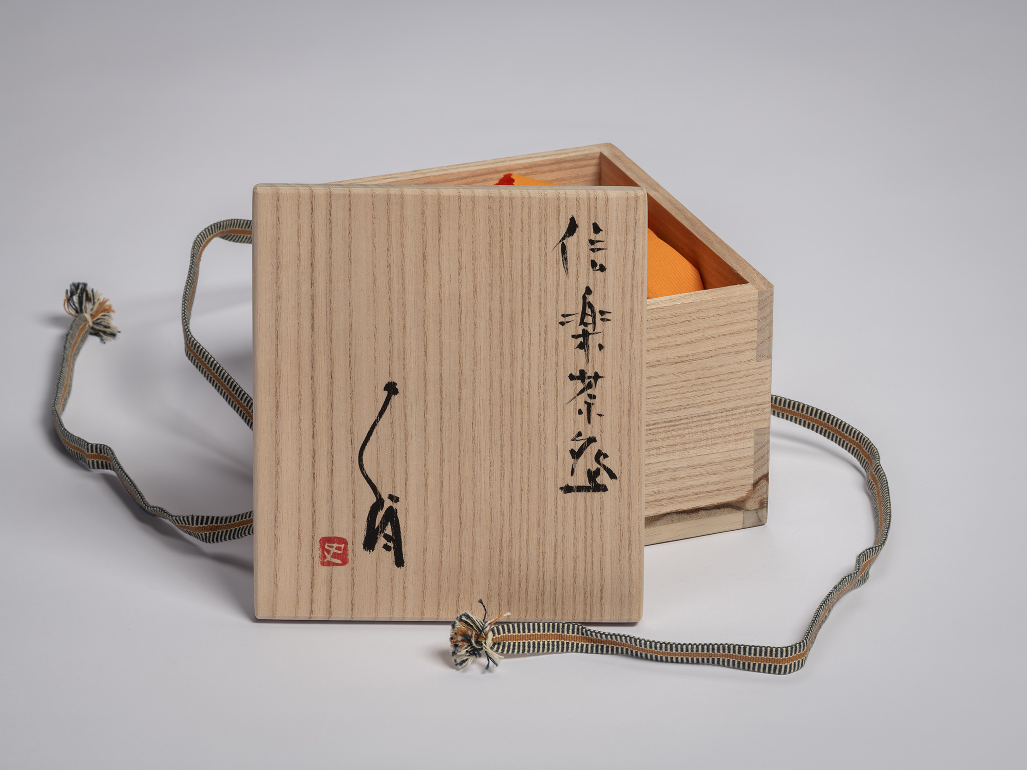 Wooden tomobako storage box for a Shigaraki tea bowl by Tsujimura, shown open with an orange cloth...