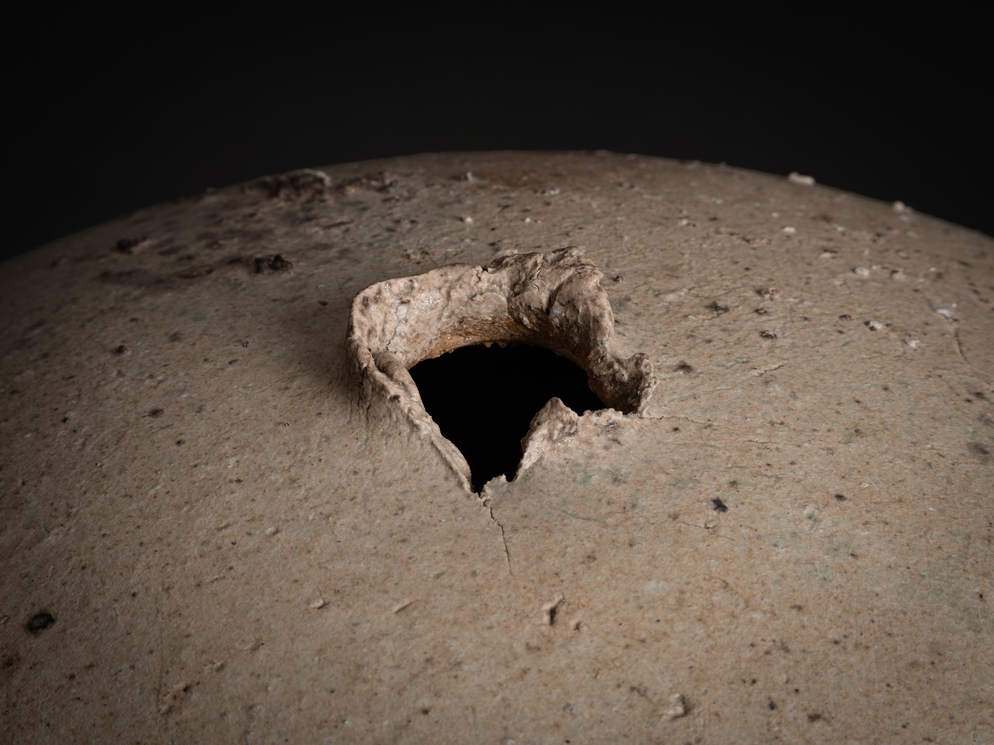 Detail of Sphere by Tsujimura showing the top opening: a small, irregular aperture with a thick,...