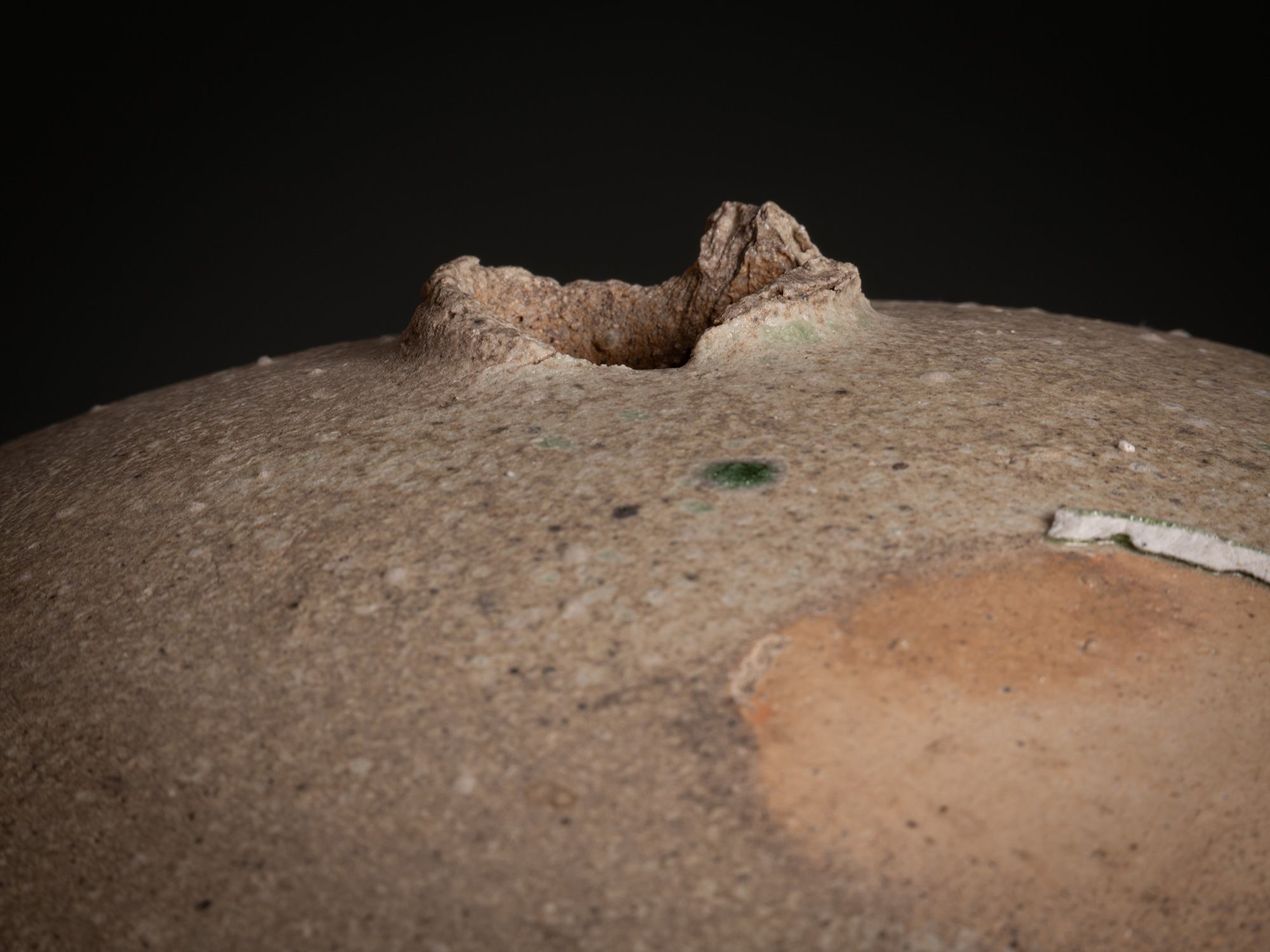 Detail of Sphere by Tsujimura showing the top opening: a small, irregular aperture with a thick,...