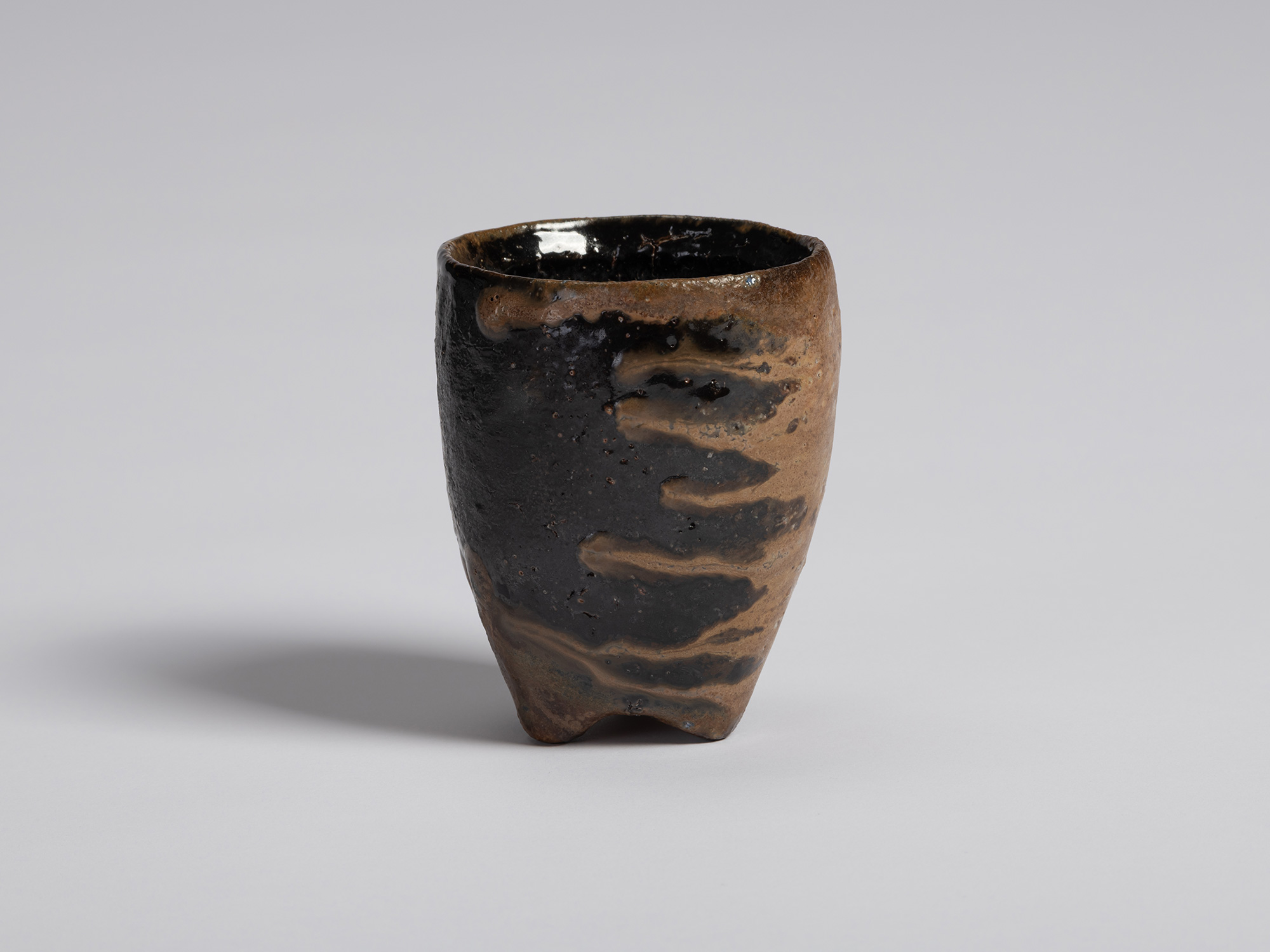 Black guinomi by Ryuichi Kakurezaki with a tall tapered form and uneven rim. The surface is dominated...