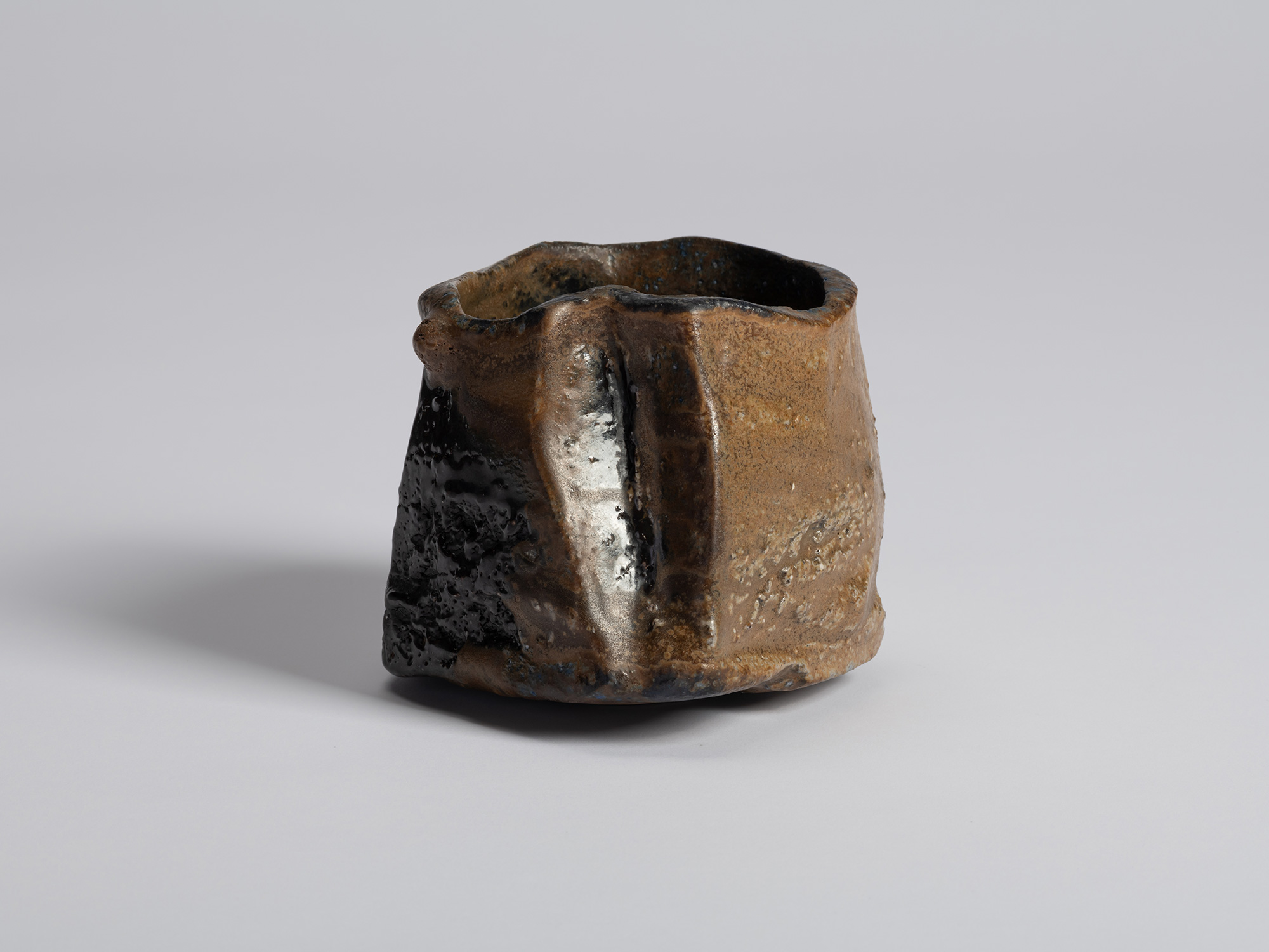Black tea bowl by Ryuichi Kakurezaki shown from an angle emphasizing the contrast between dark...