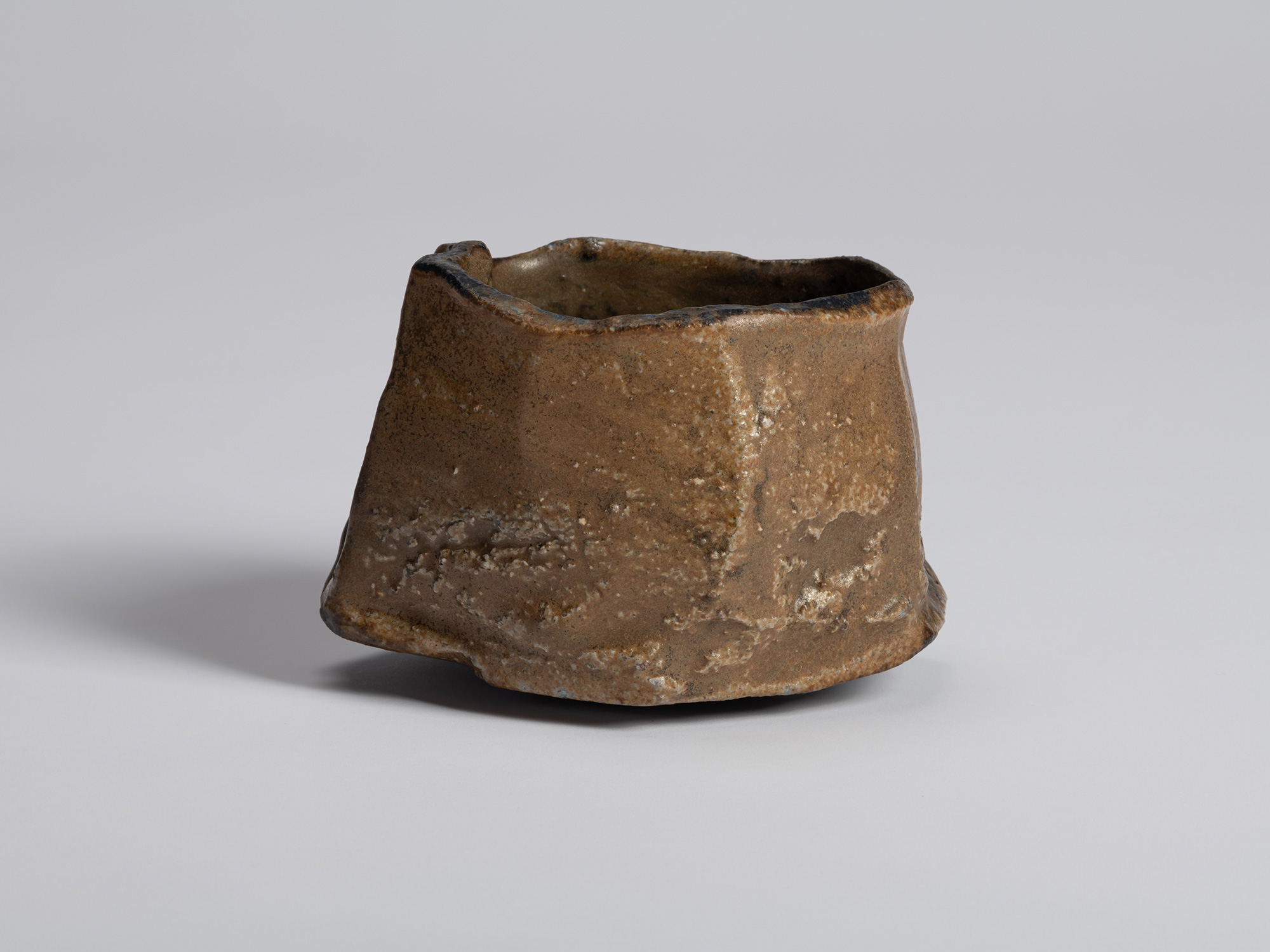 Black tea bowl by Ryuichi Kakurezaki viewed from a side dominated by exposed brown clay. The surface...