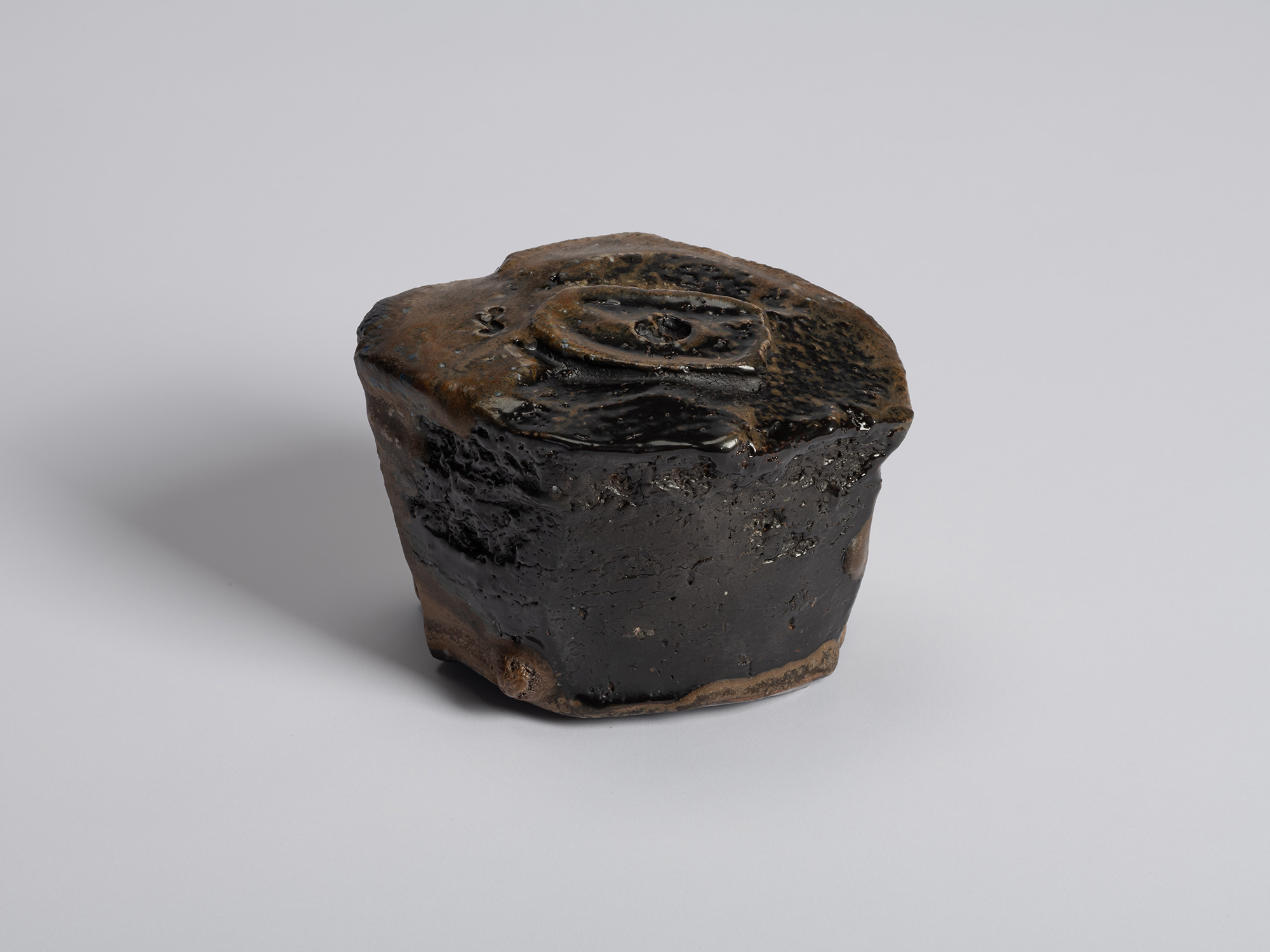 Foot view of a black tea bowl by Ryuichi Kakurezaki showing a rugged, asymmetrical base with thick...
