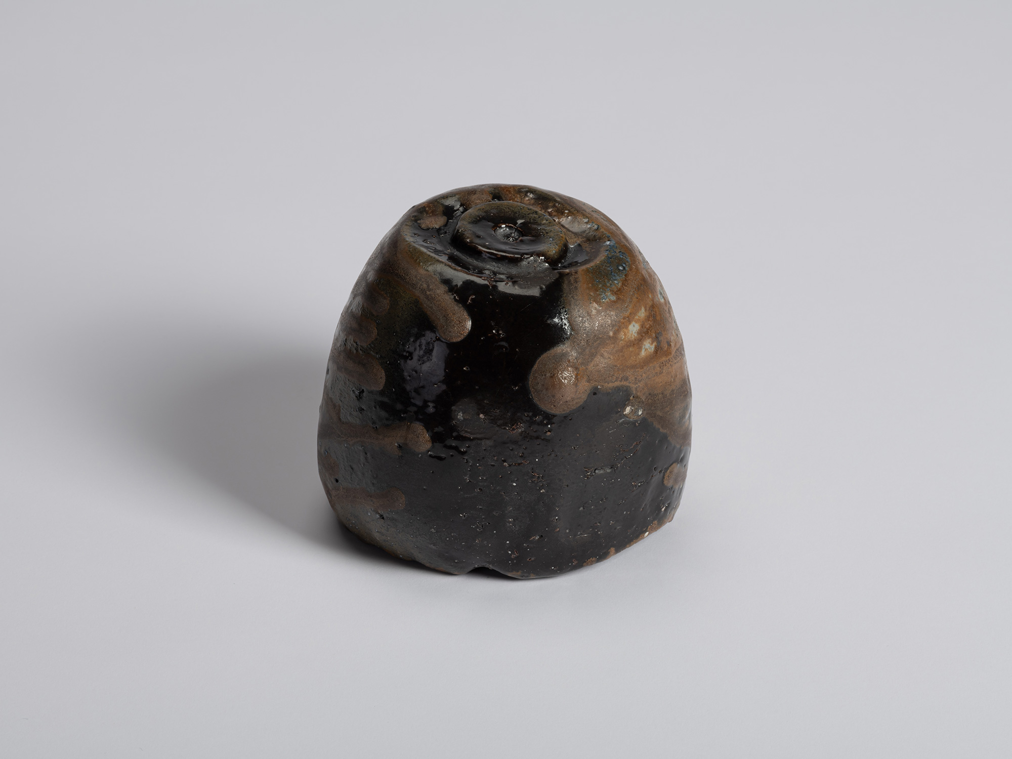 Foot view of a black tea bowl by Ryuichi Kakurezaki showing a rounded base with glossy black firing...