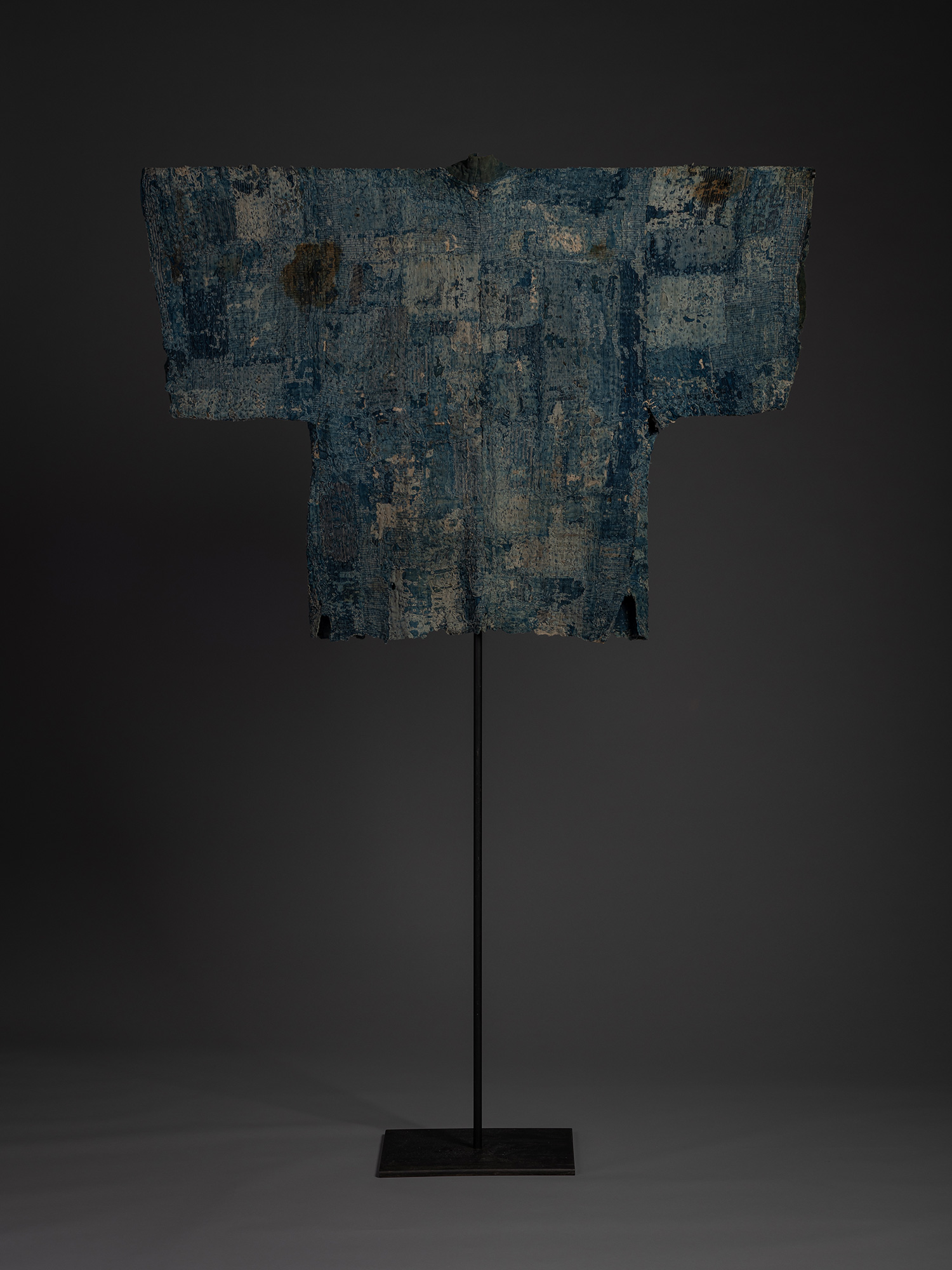 Full rear installation view of a Japanese boro hanten on a black metal stand. The garment is composed...