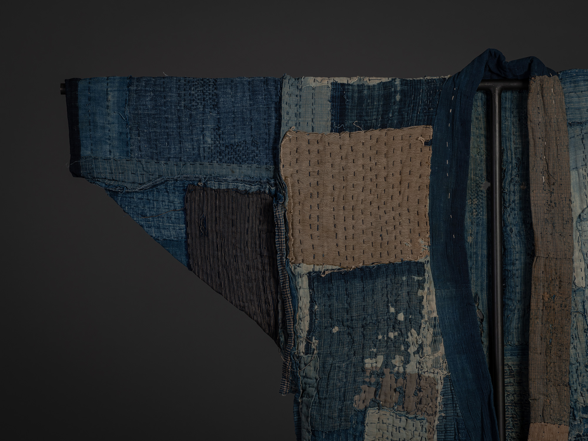 Close-up of the left shoulder and collar area showing heavily patched indigo cotton panels and...