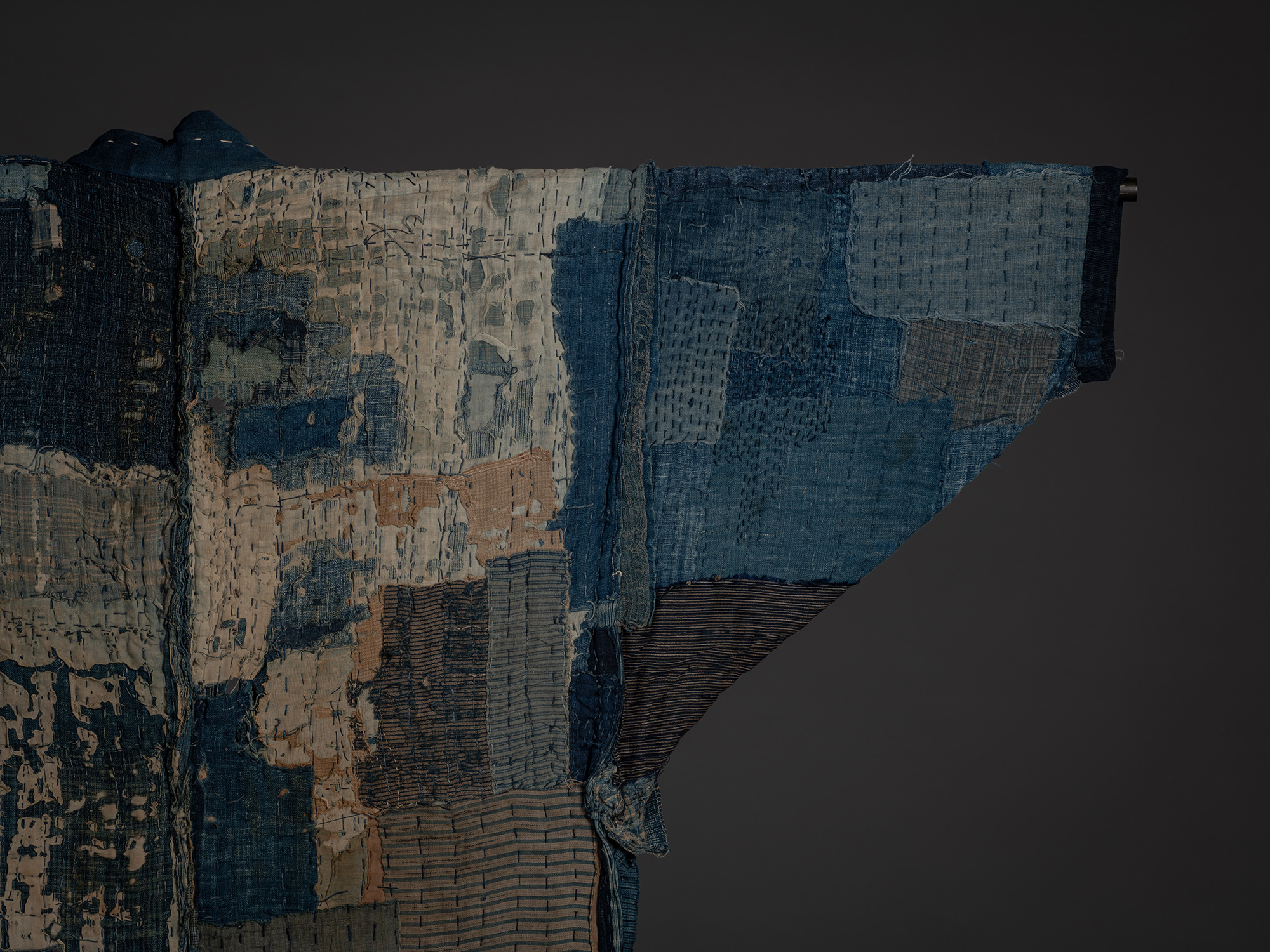 Detail of the opposite shoulder and sleeve featuring pale blue, indigo, and striped cotton fragments...