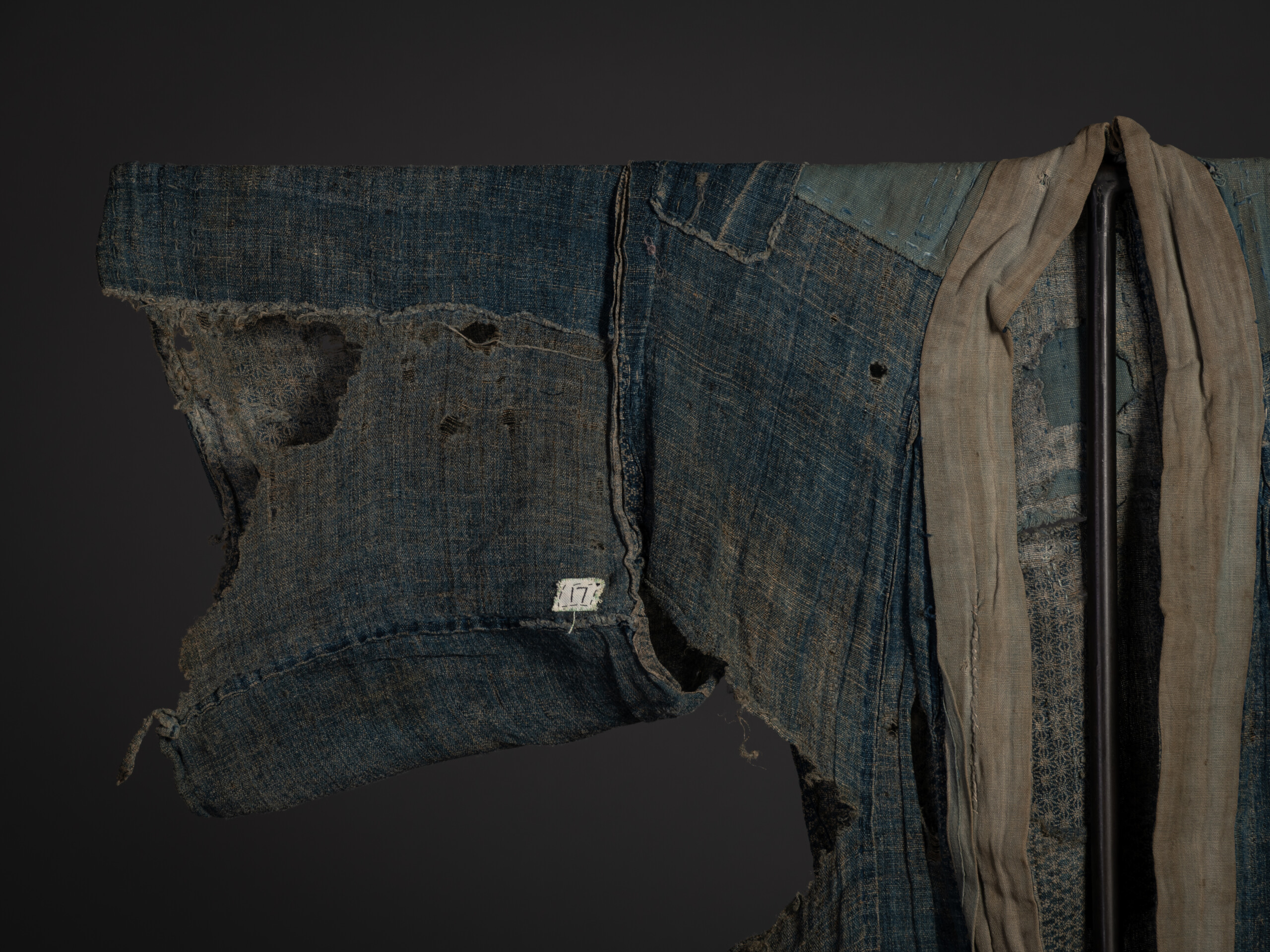 Close-up of the kimono's sleeve and upper torso, showing heavily worn indigo hemp or ramie fabric...