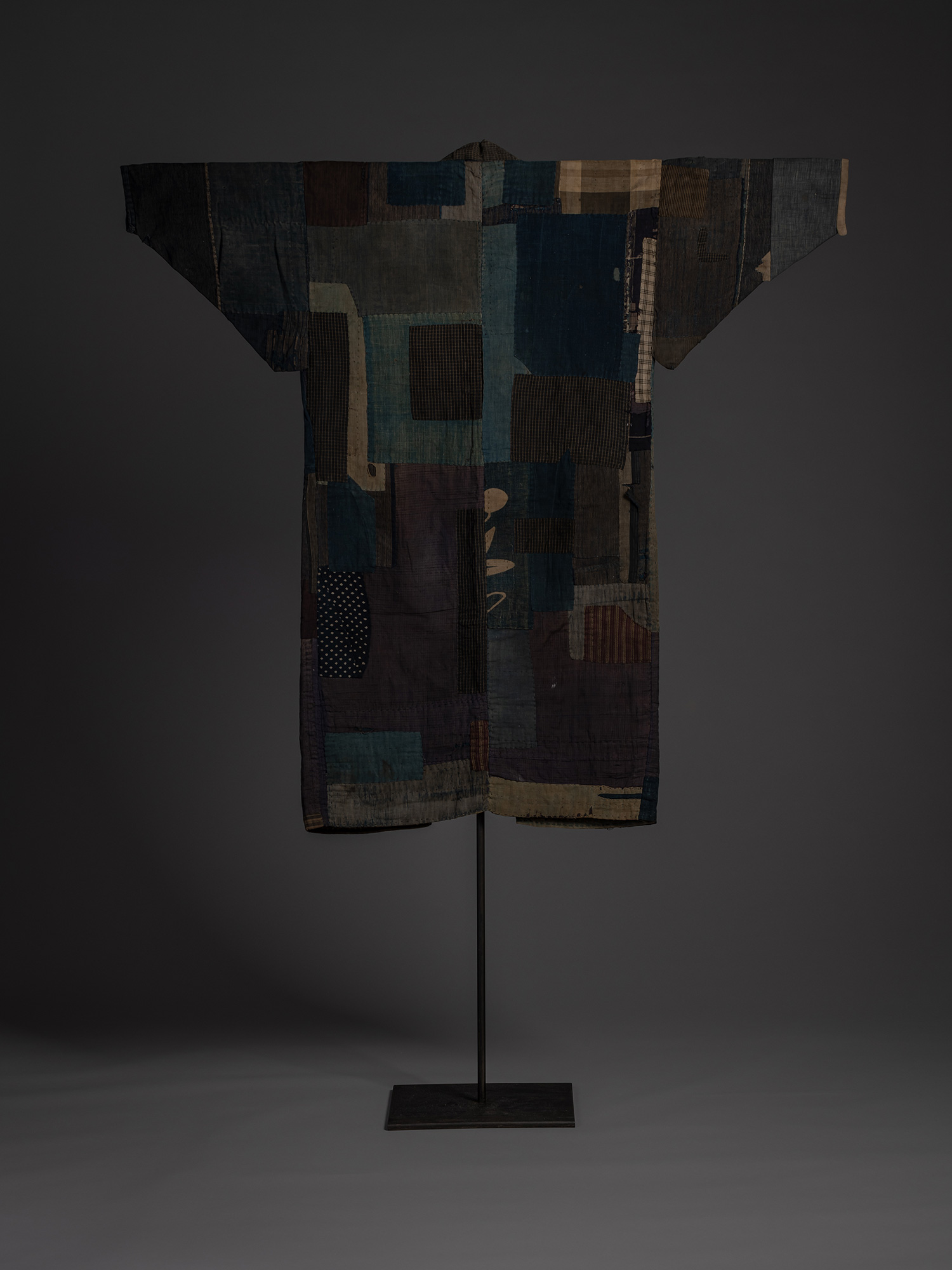 Full back view of a Japanese boro kimono displayed on a stand. The garment is composed of large...