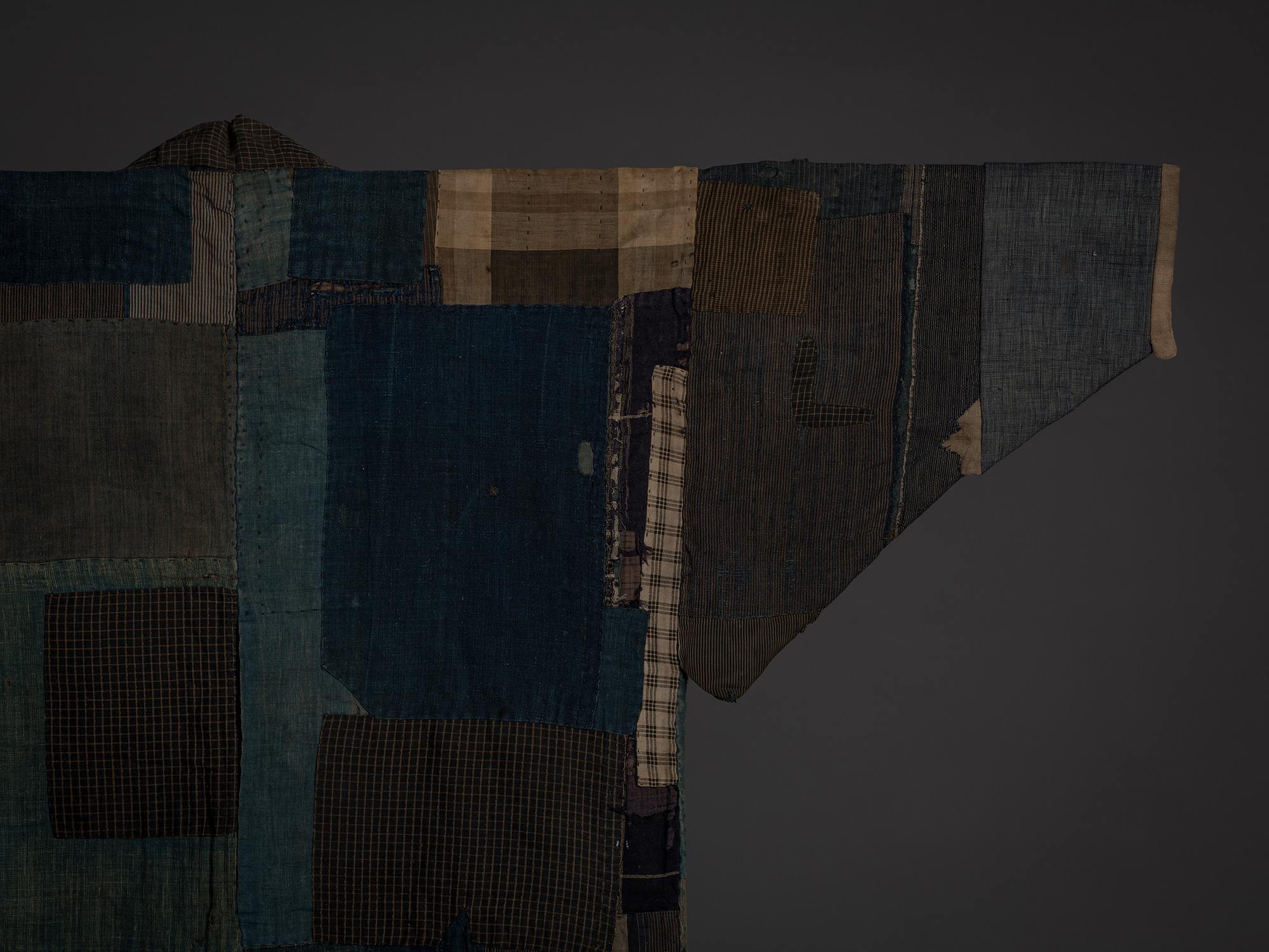 Close-up of the back right shoulder and sleeve showing an arrangement of indigo, brown, gray, and...