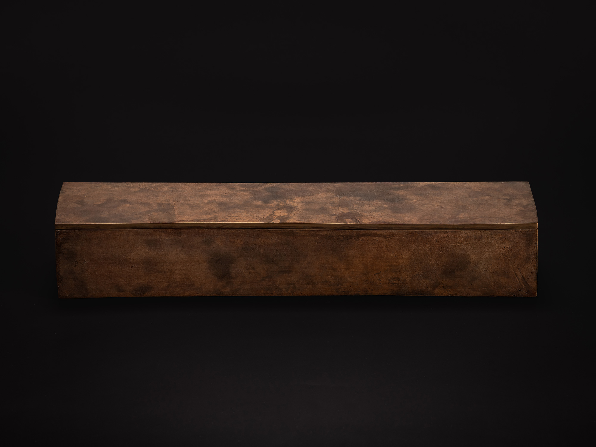 Rectangular bronze box with a gently curved lid resting on a black background. The surface has...