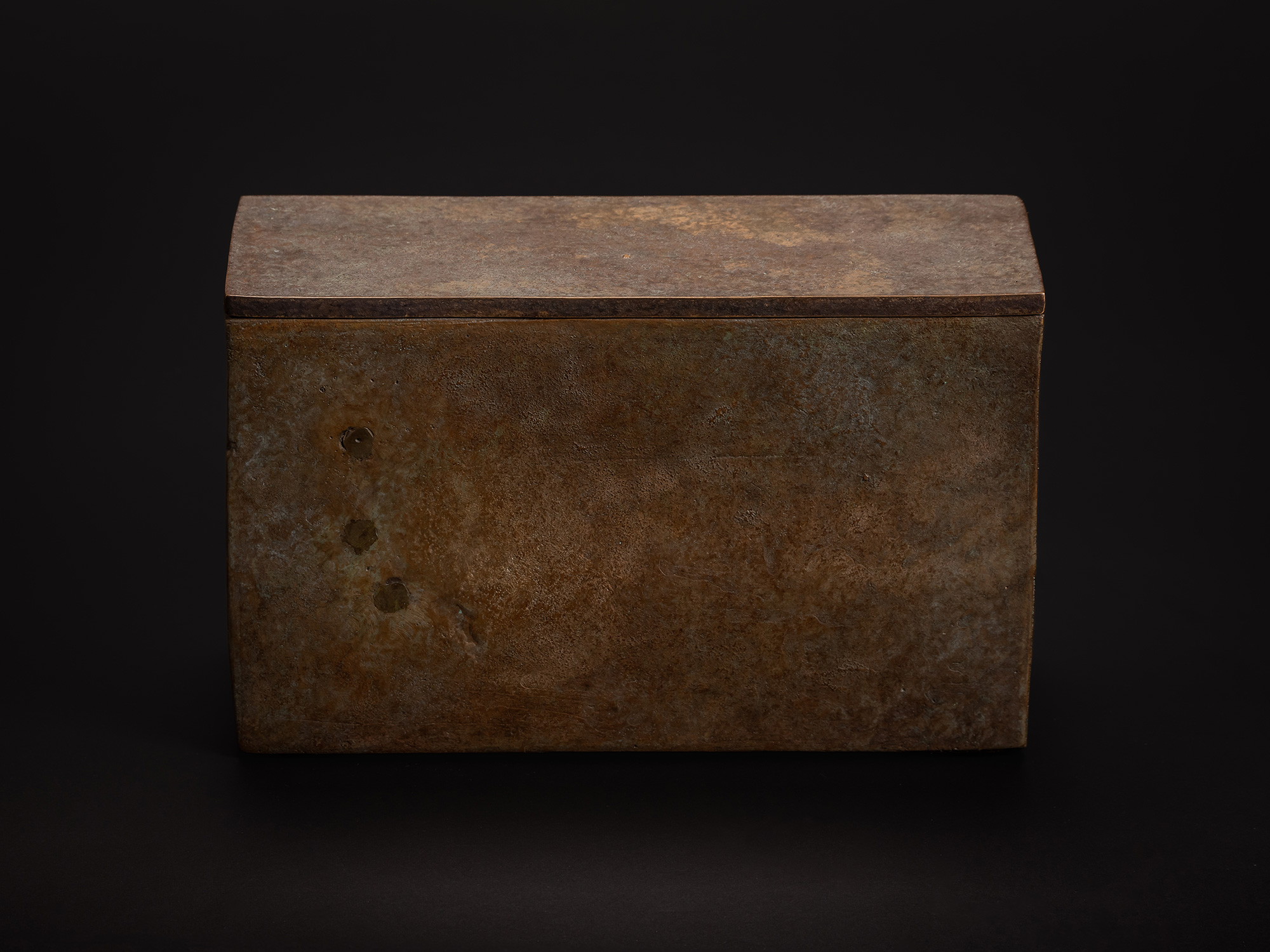 Rectangular bronze box with a flat lid shown against a black background. The surface displays a...