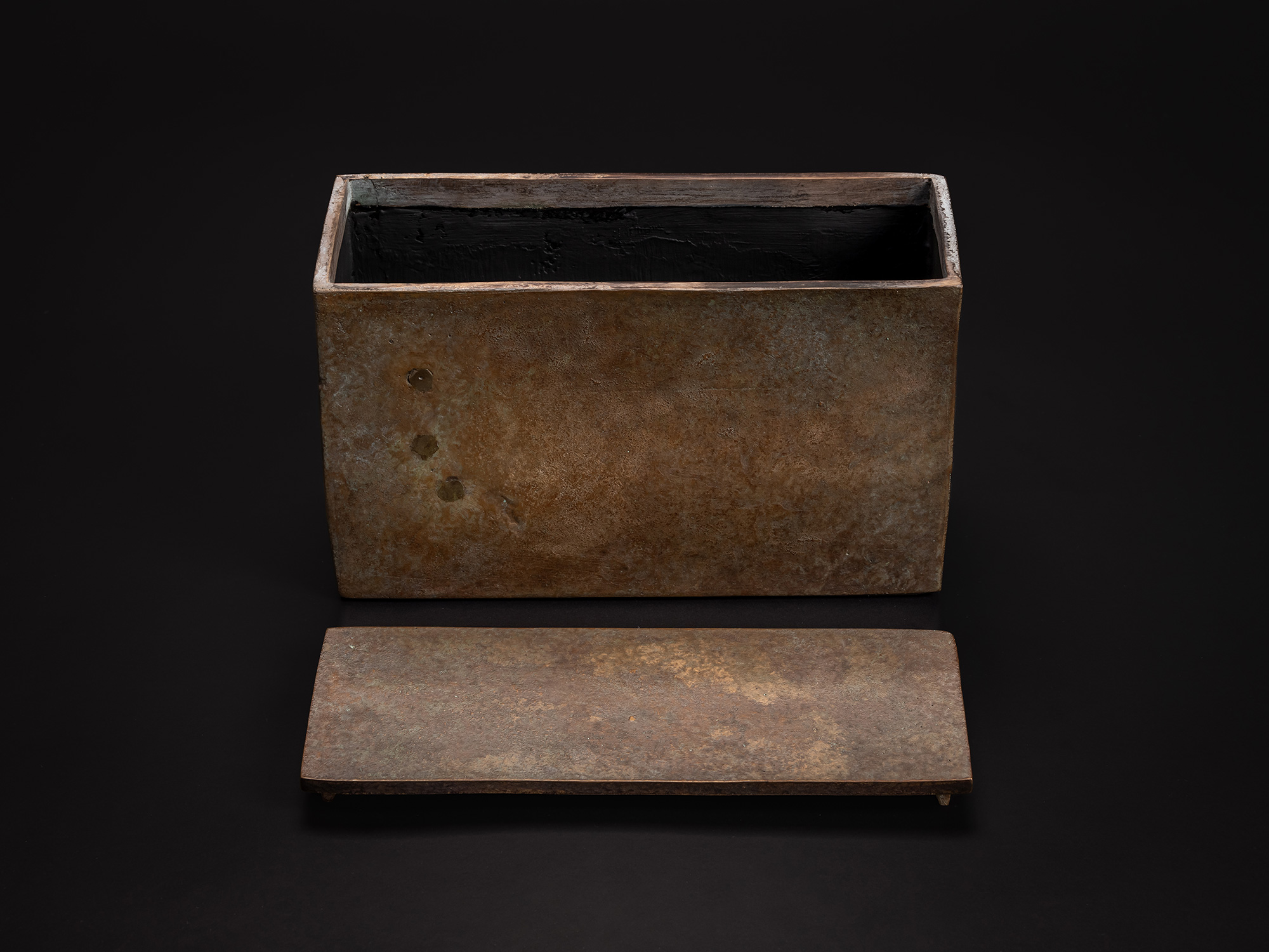 Bronze box displayed with its lid removed and placed in front. The rectangular interior is finished...