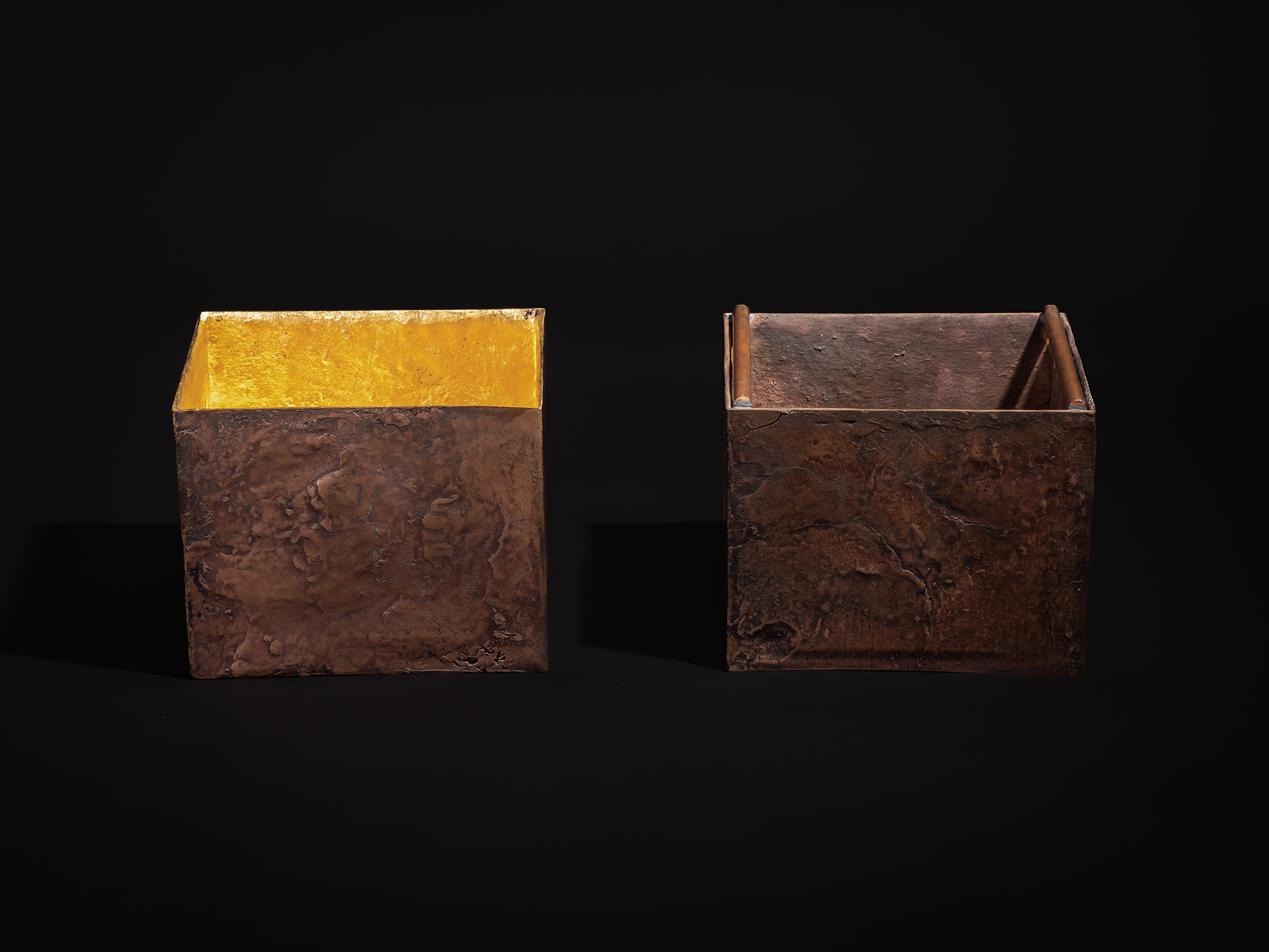 A straight-on, eye-level view of Koji Hatakeyama's bronze box Doing Little - Large against a dark...