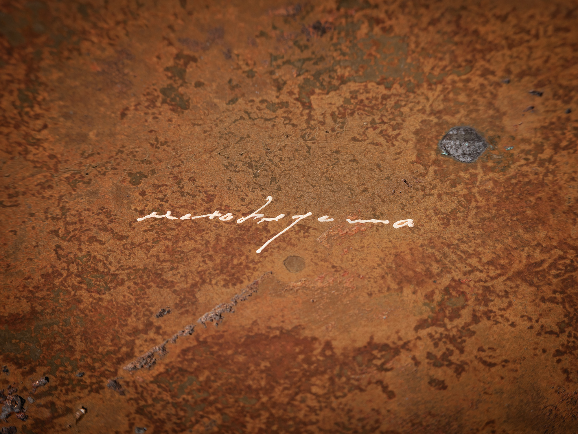 A macro, close-up view focusing on Koji Hatakeyama's incised signature on the bronze surface of...