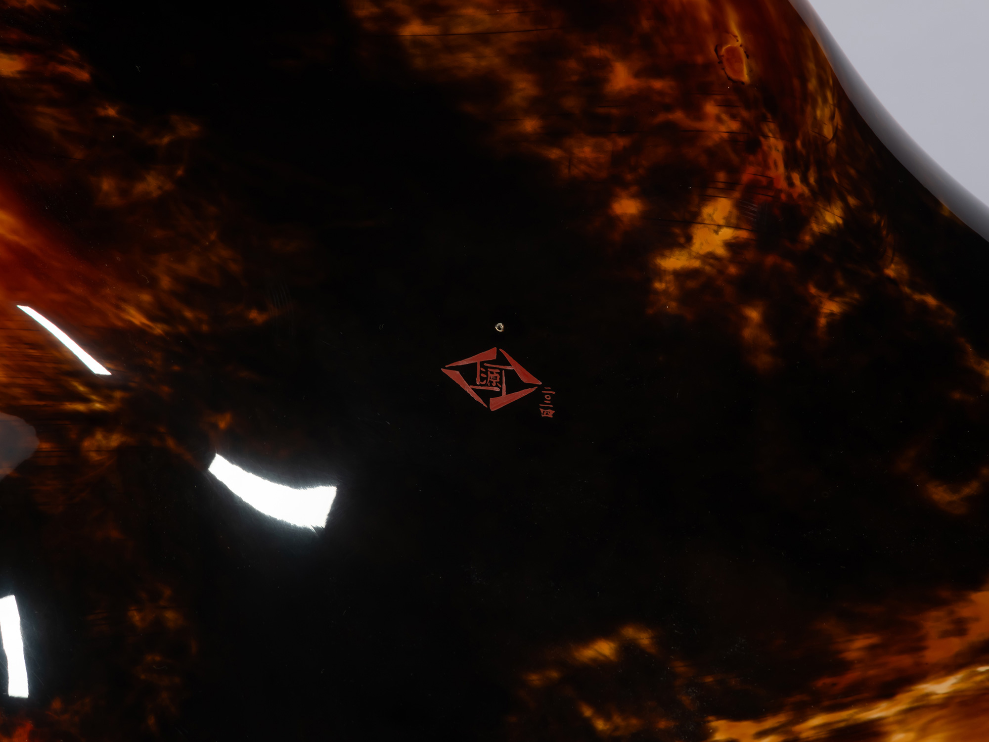 A macro close-up view of Genta Ishizuka’s artist signature on the dark lacquer underside of the...