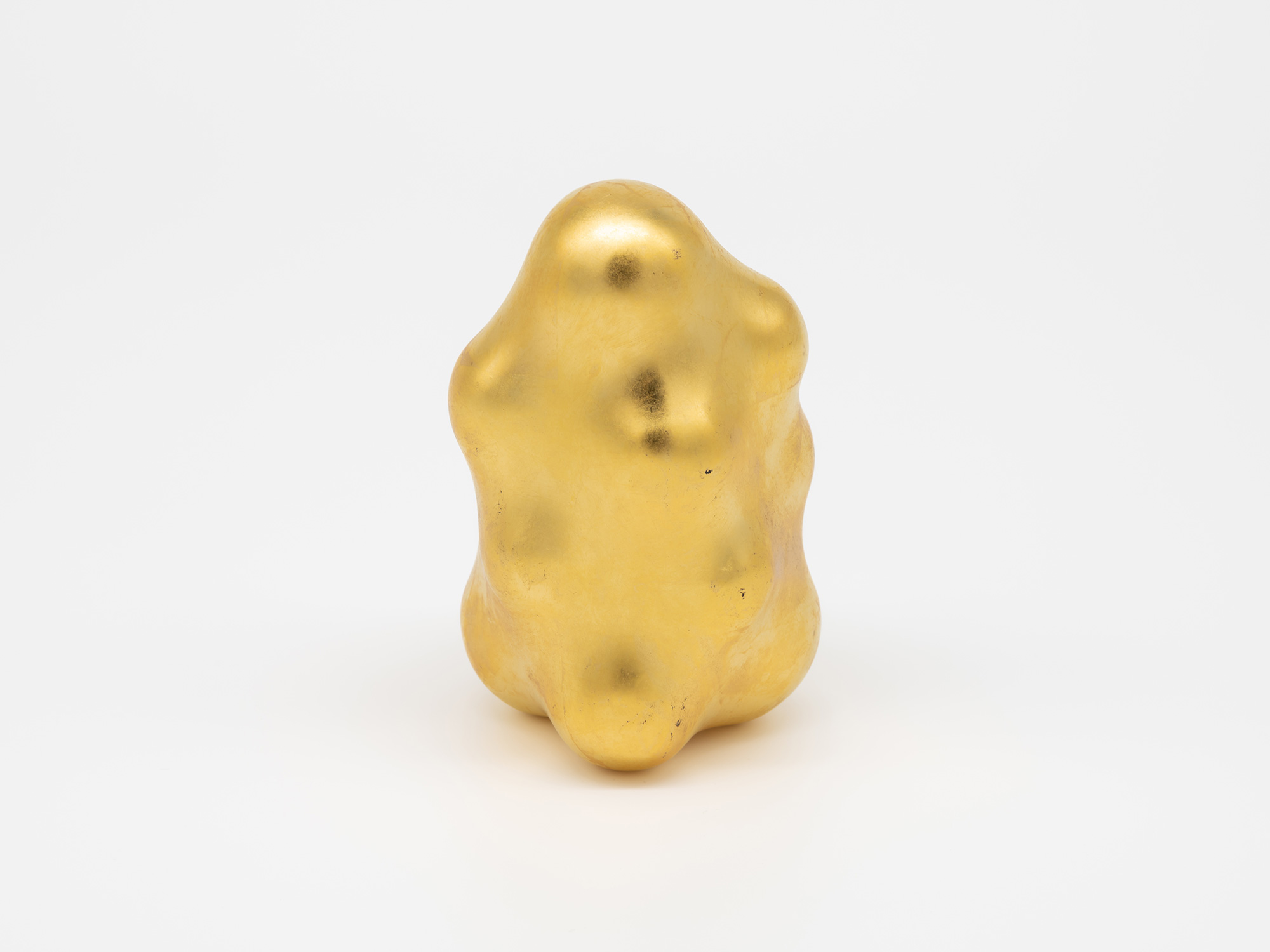 A side profile view of Genta Ishizuka's Untitled gold sculpture against a plain white background....