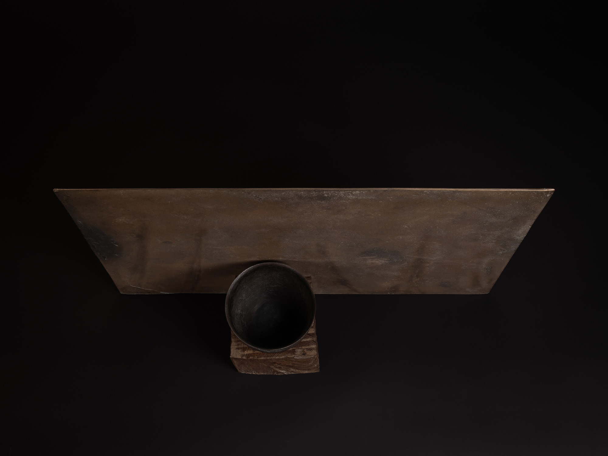 Aerial view of a bronze artwork by Koji Hatakeyama featuring a dark circular vessel resting on...