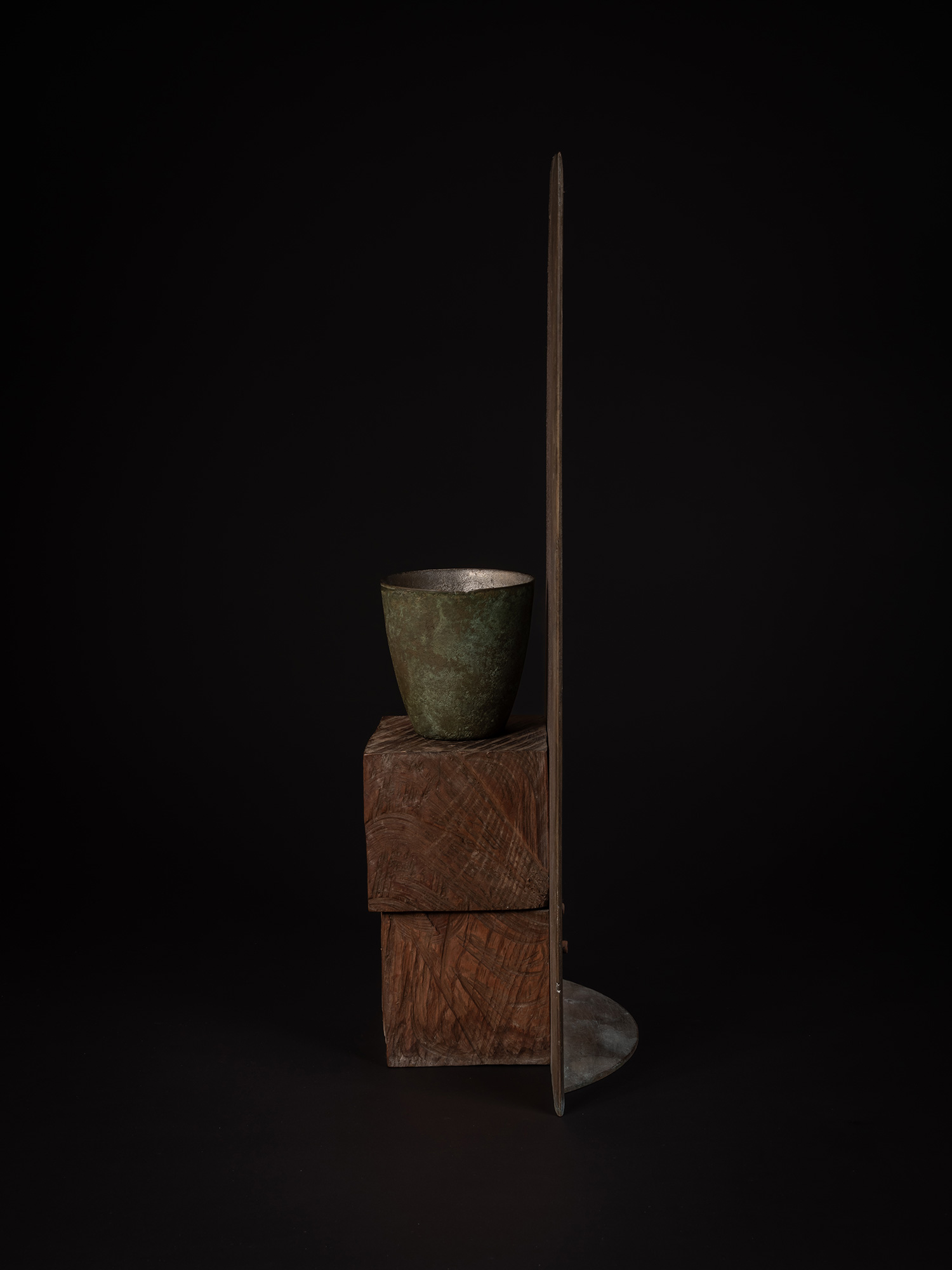 Side profile of a bronze artwork by Koji Hatakeyama showing a narrow green-patinated bronze vessel...