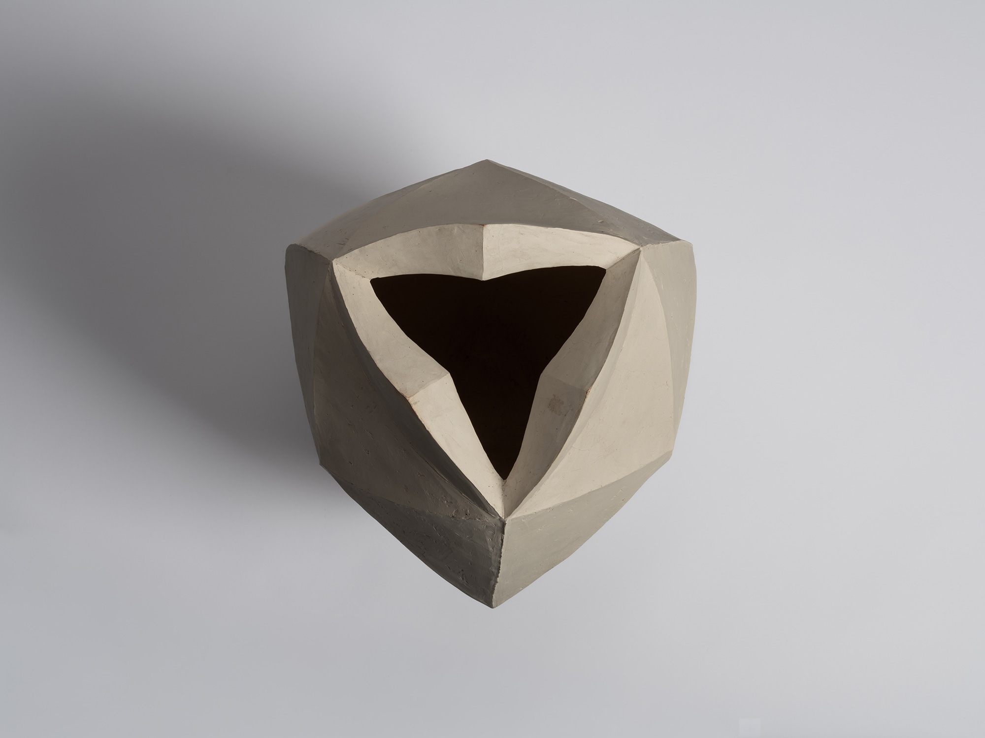 An overhead, top-down view of an unglazed, off-white stoneware vase. The camera looks directly...
