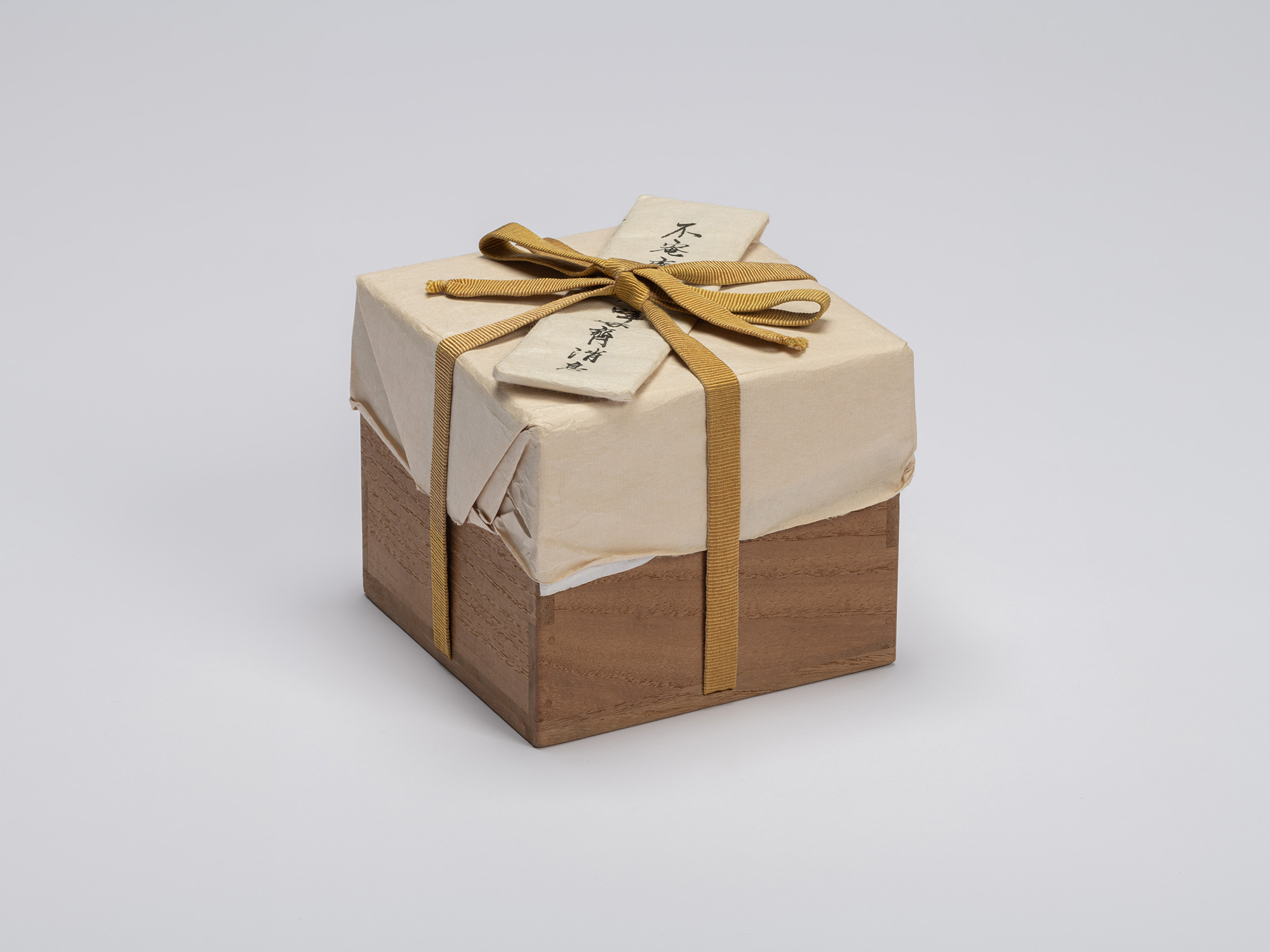 A square, medium-toned paulownia wood innermost storage box (tomobako) sits centered against a...