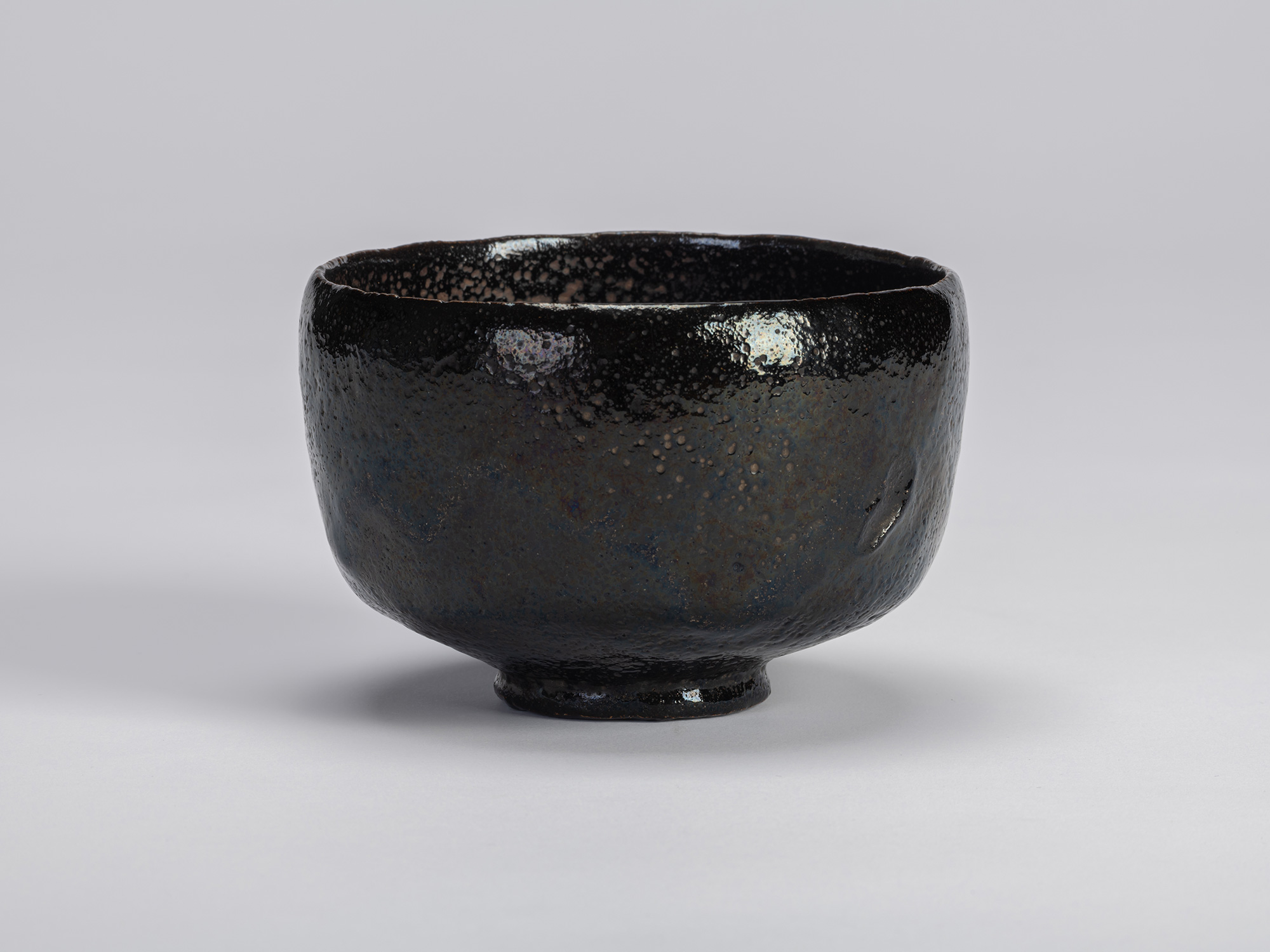The historic black Raku tea bow named Yokogumo (Horizontal Cloud)l rests centered against a seamless...