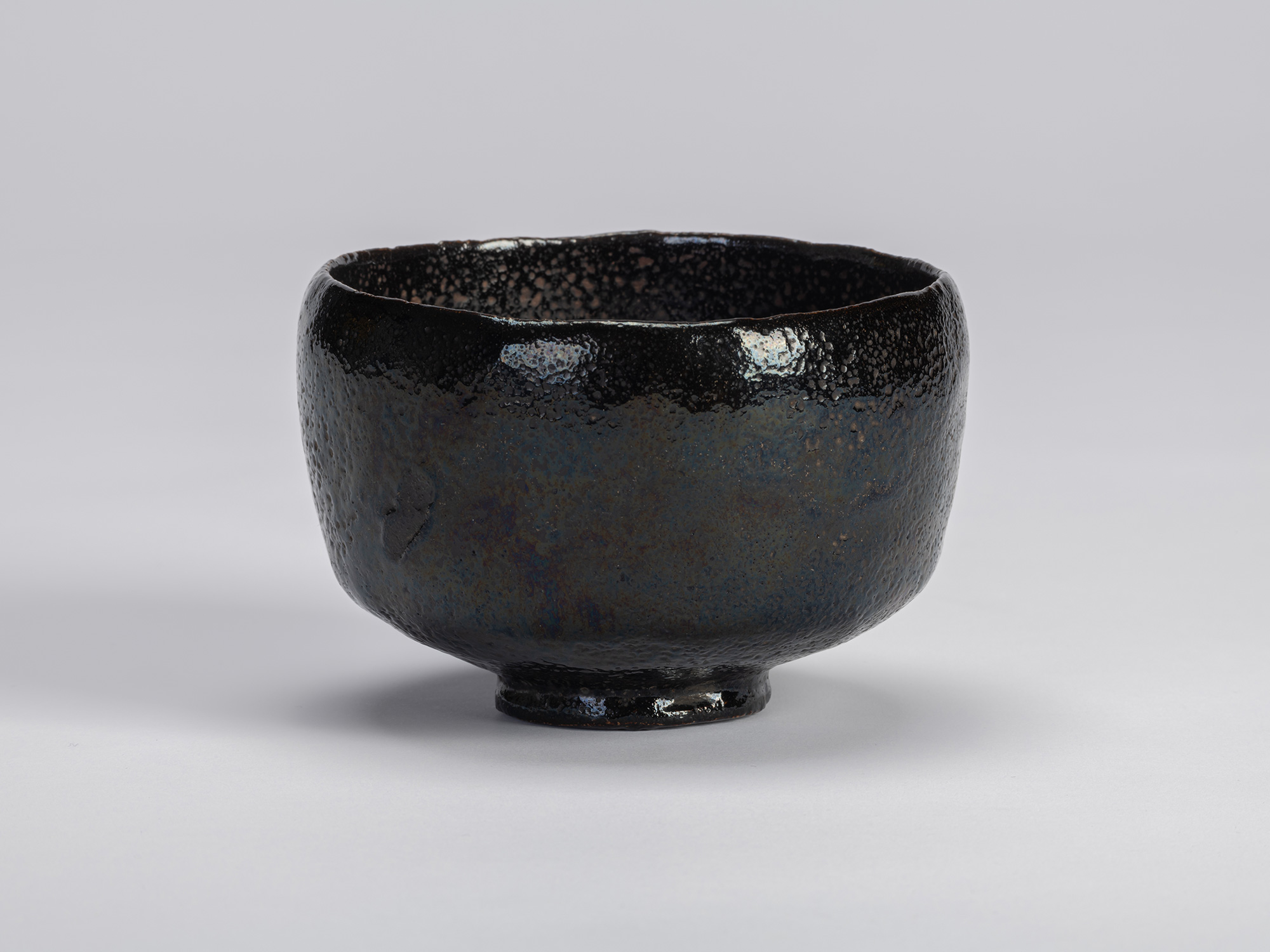 The historic black Raku tea bow named Yokogumo (Horizontal Cloud)l rests centered against a seamless...