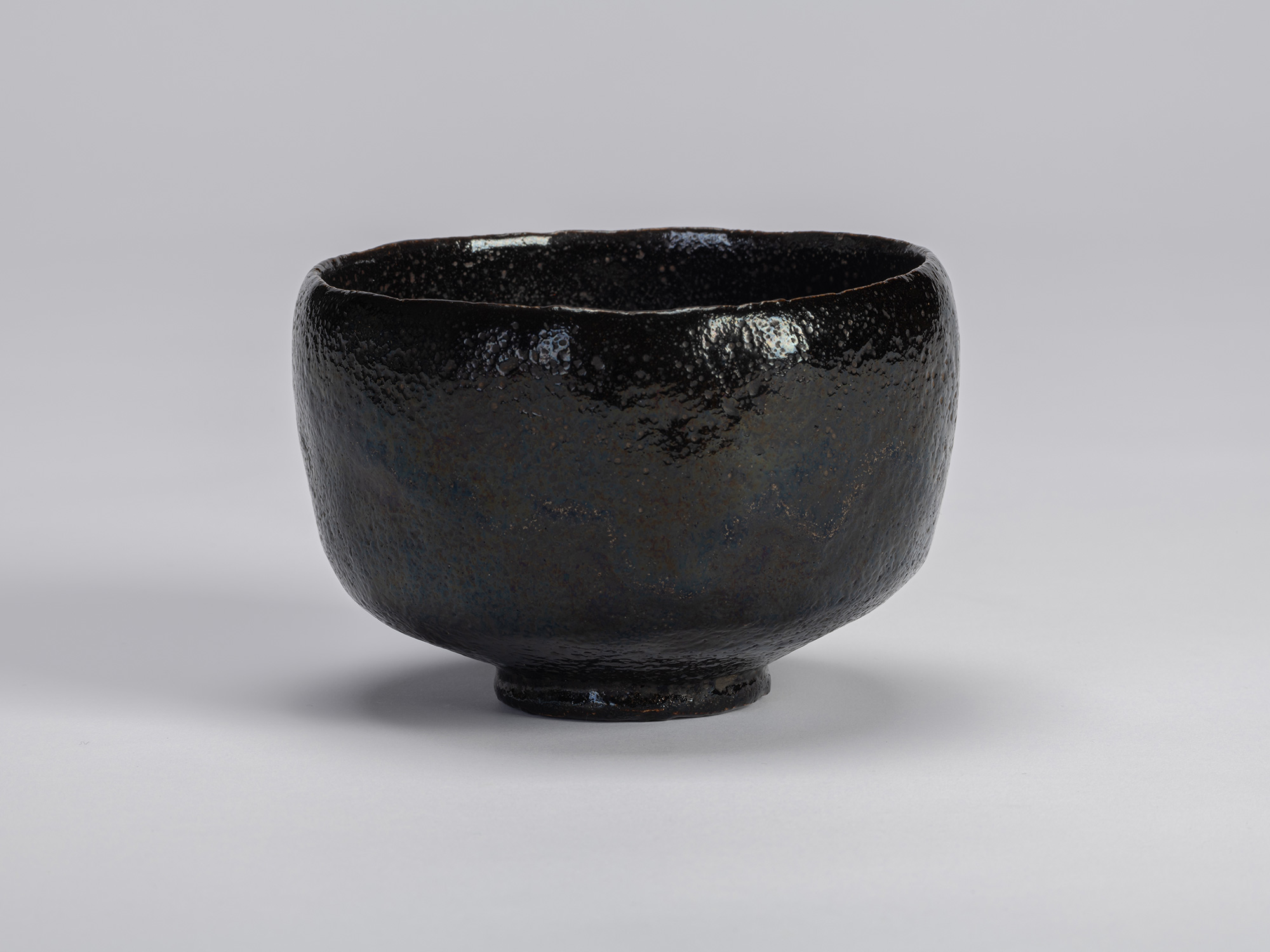 The historic black Raku tea bow named Yokogumo (Horizontal Cloud)l rests centered against a seamless...