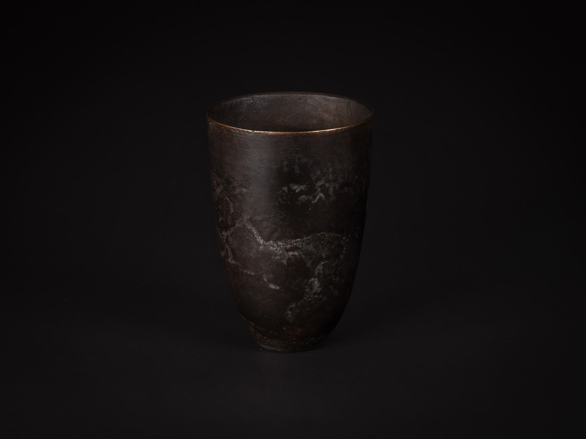Three-quarter view of bronze as Bronze No. 9. The vessel’s rounded body narrows toward the base,...