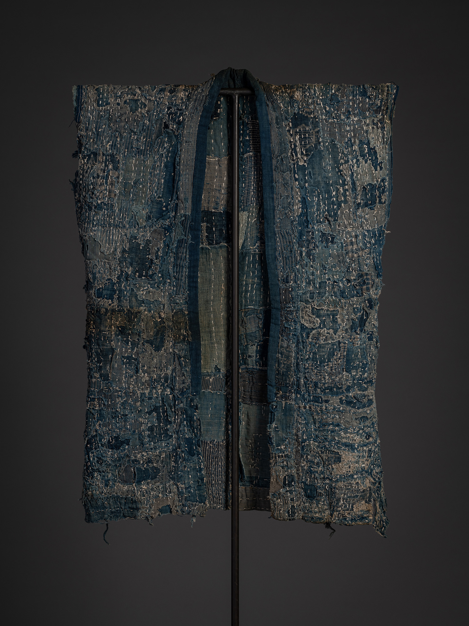 Full front view of a boro work coat made from cotton and hemp. The garment hangs open on a black...